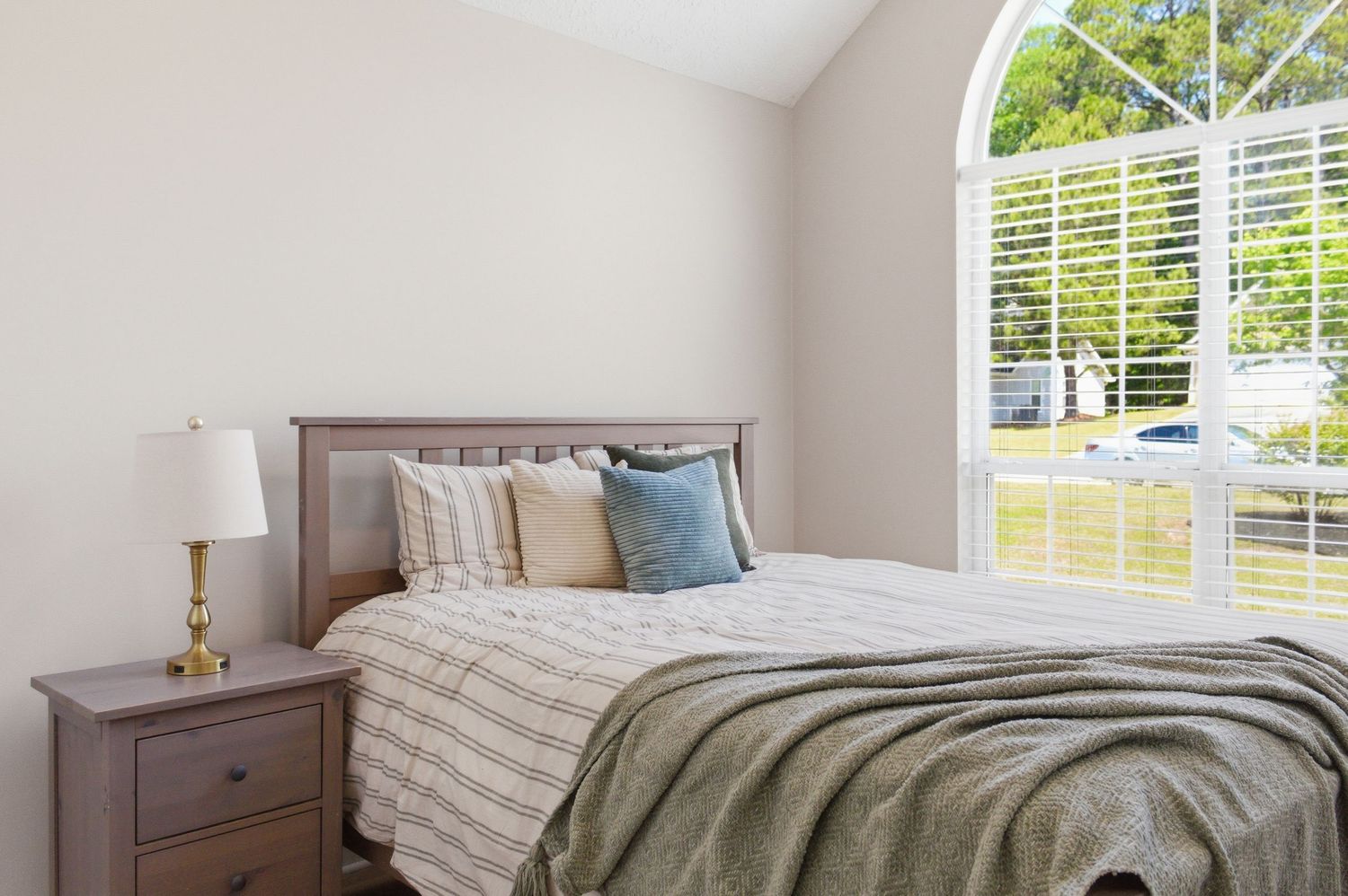 Cozy bedroom with wooden headboard, striped bedding, blue accent pillows, and arched window with natural light.