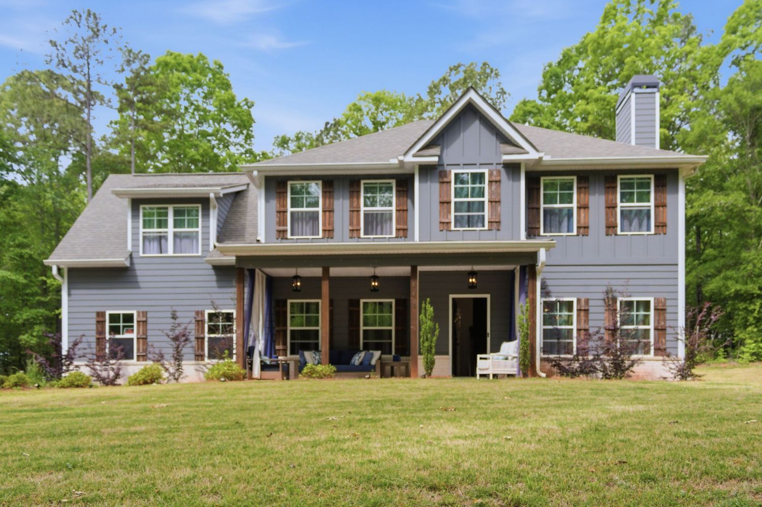 Gray two-story craftsman home with covered front porch, shutters, and lush green lawn.