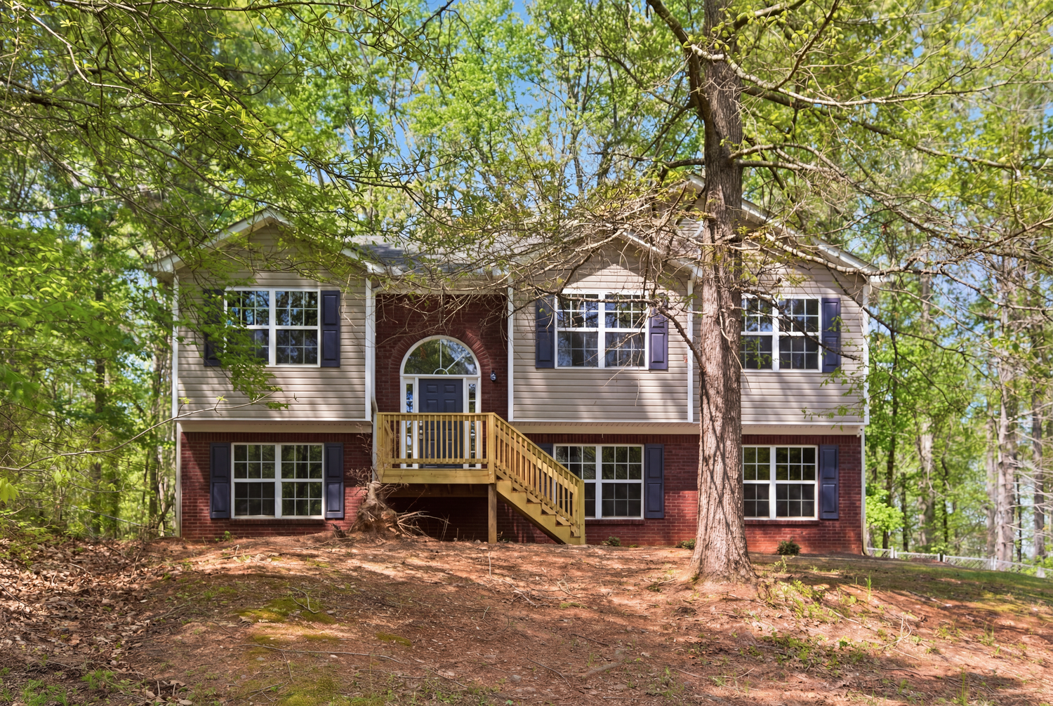 Two-story home with brick lower level, gray siding, yellow staircase, and arched window surrounded by tall trees.