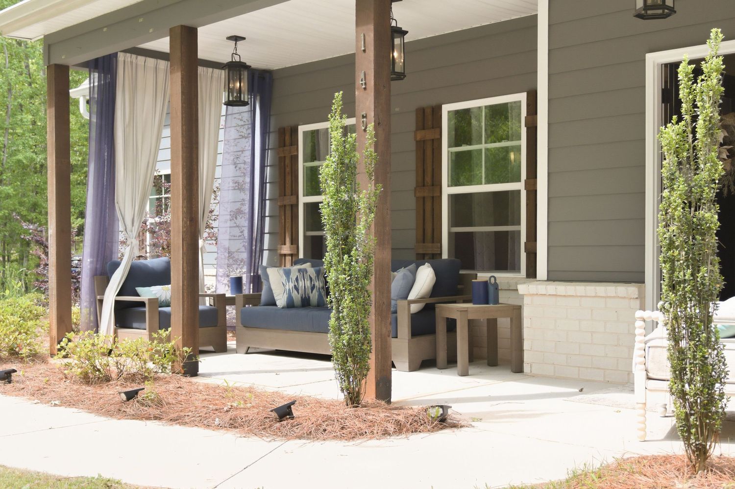 Charming covered front porch with navy blue outdoor furniture, tall wooden columns, and lush landscaping.