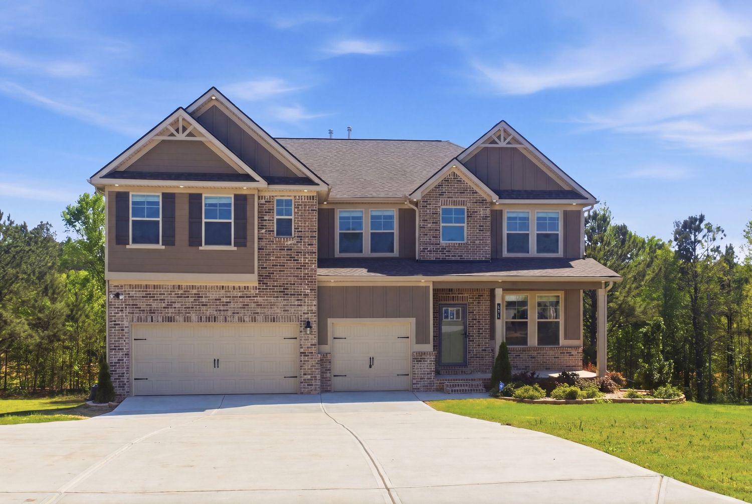 Two-story brick and stone home with three-car garage, manicured lawn, and tree-lined backdrop under blue skies.