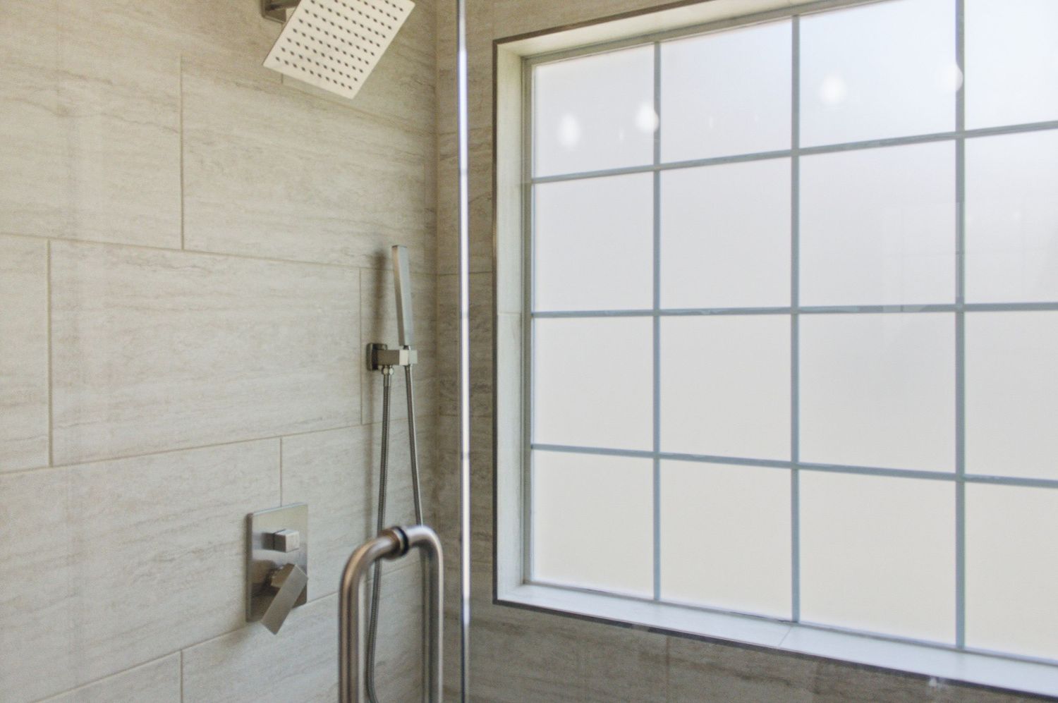 Walk-in shower with rainfall showerhead, handheld sprayer, gray stone tiles, and frosted grid privacy window.