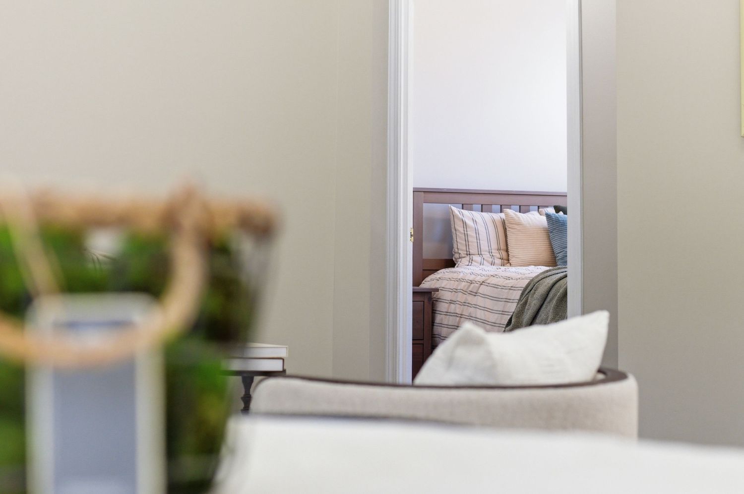 Elegant bedroom reflected in a mirror, showcasing neutral tones, layered pillows, and cozy bedding.