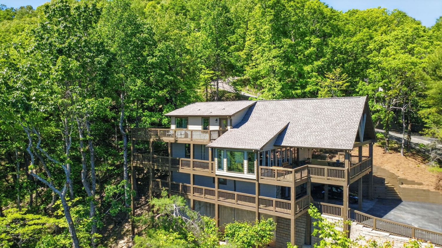 Aerial view of a multi-level mountain home with large decks surrounded by lush green trees.