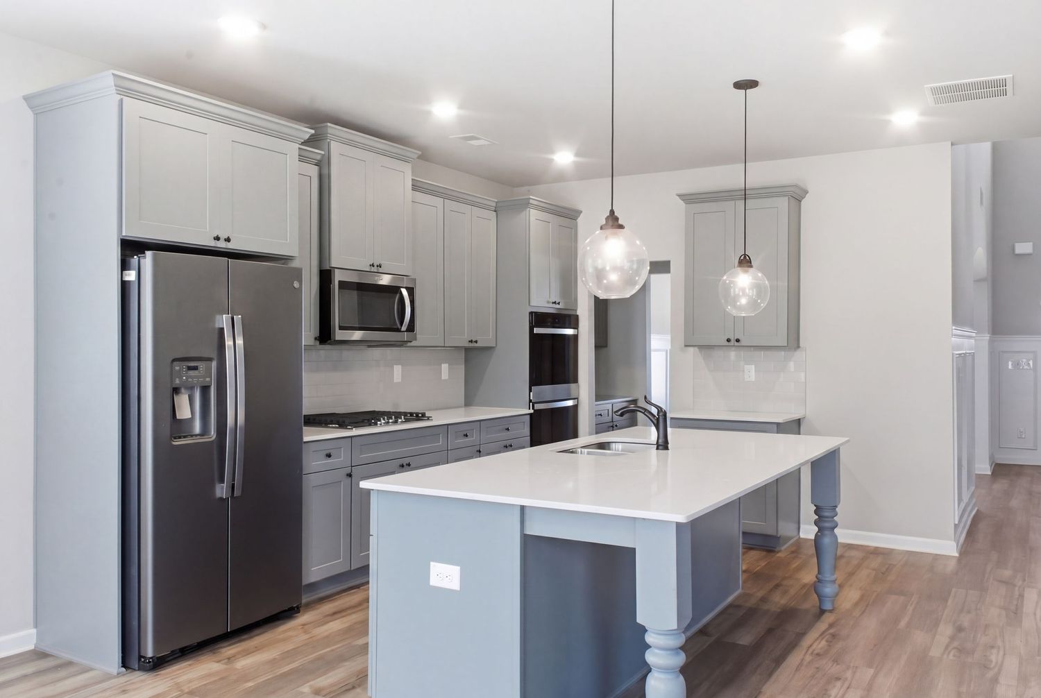Modern kitchen with gray cabinets, stainless steel appliances, white quartz island, pendant lights, and hardwood floors.
