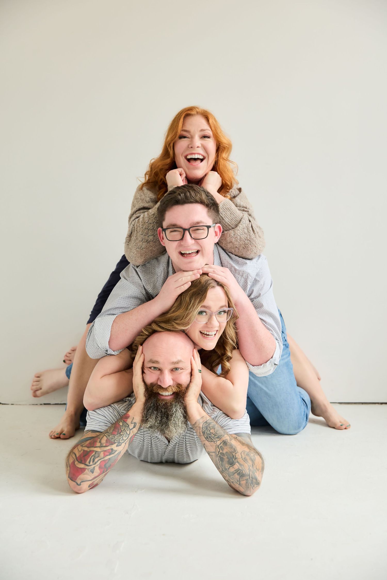Four friends pose in a playful human stack formation, laughing and smiling against a white studio background.