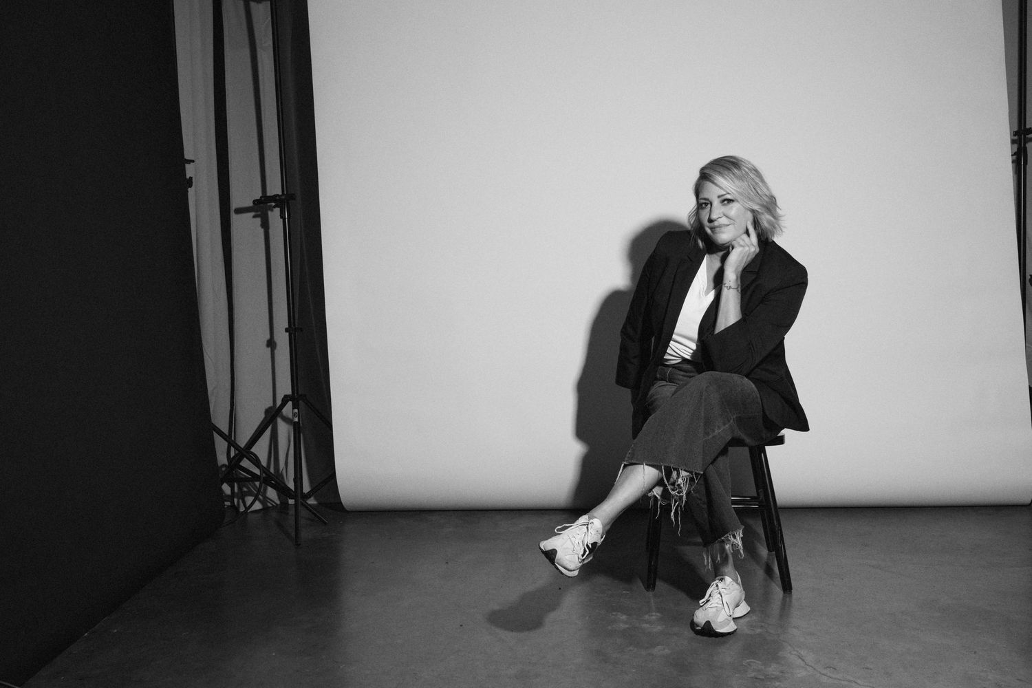 A black and white studio portrait showing relaxed seated pose against white backdrop.