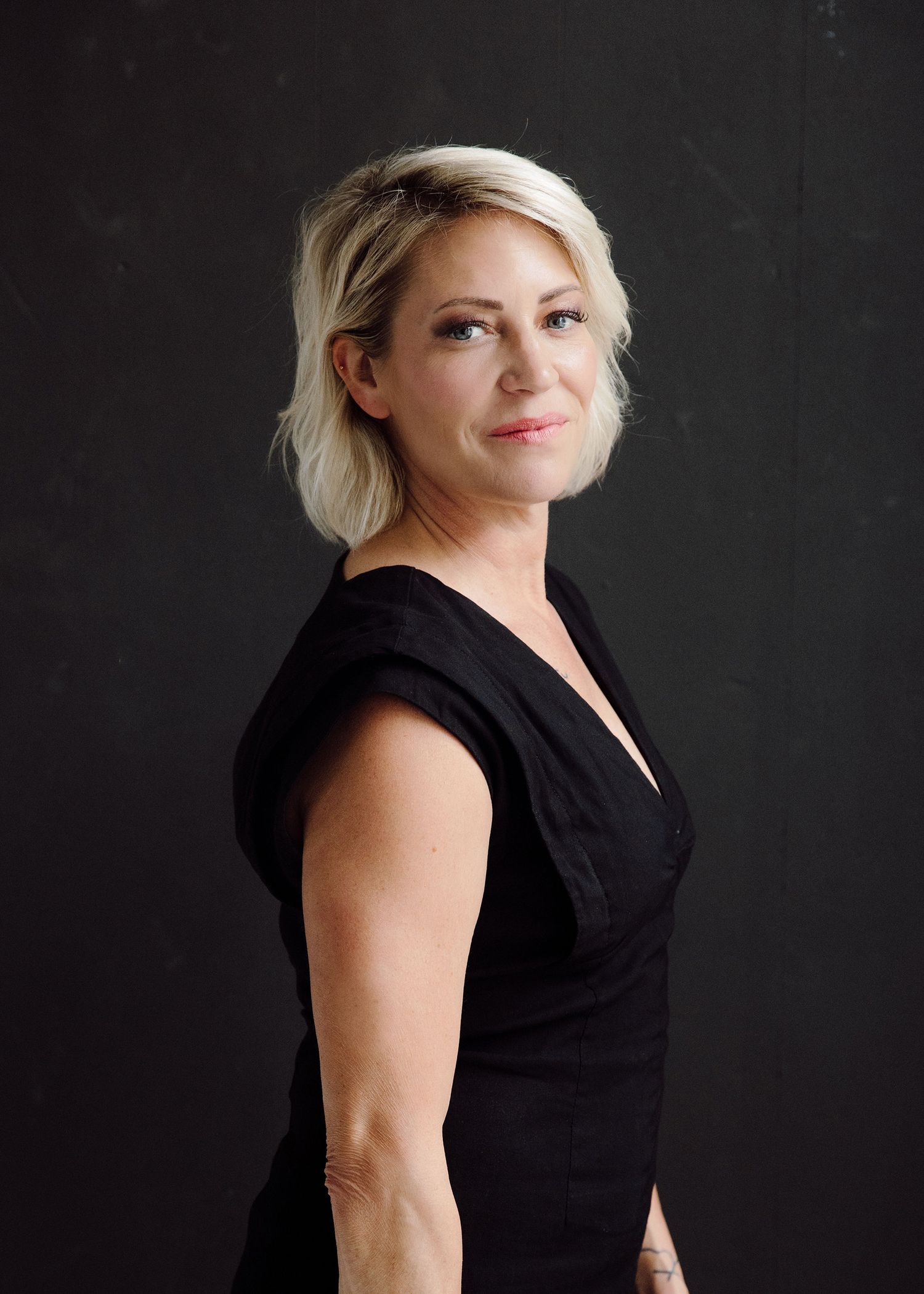 Portrait series of woman in black sleeveless dress against dark background.