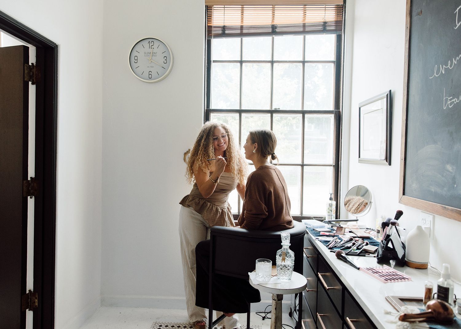 Two people work together at a desk near a window in a bright white office space.