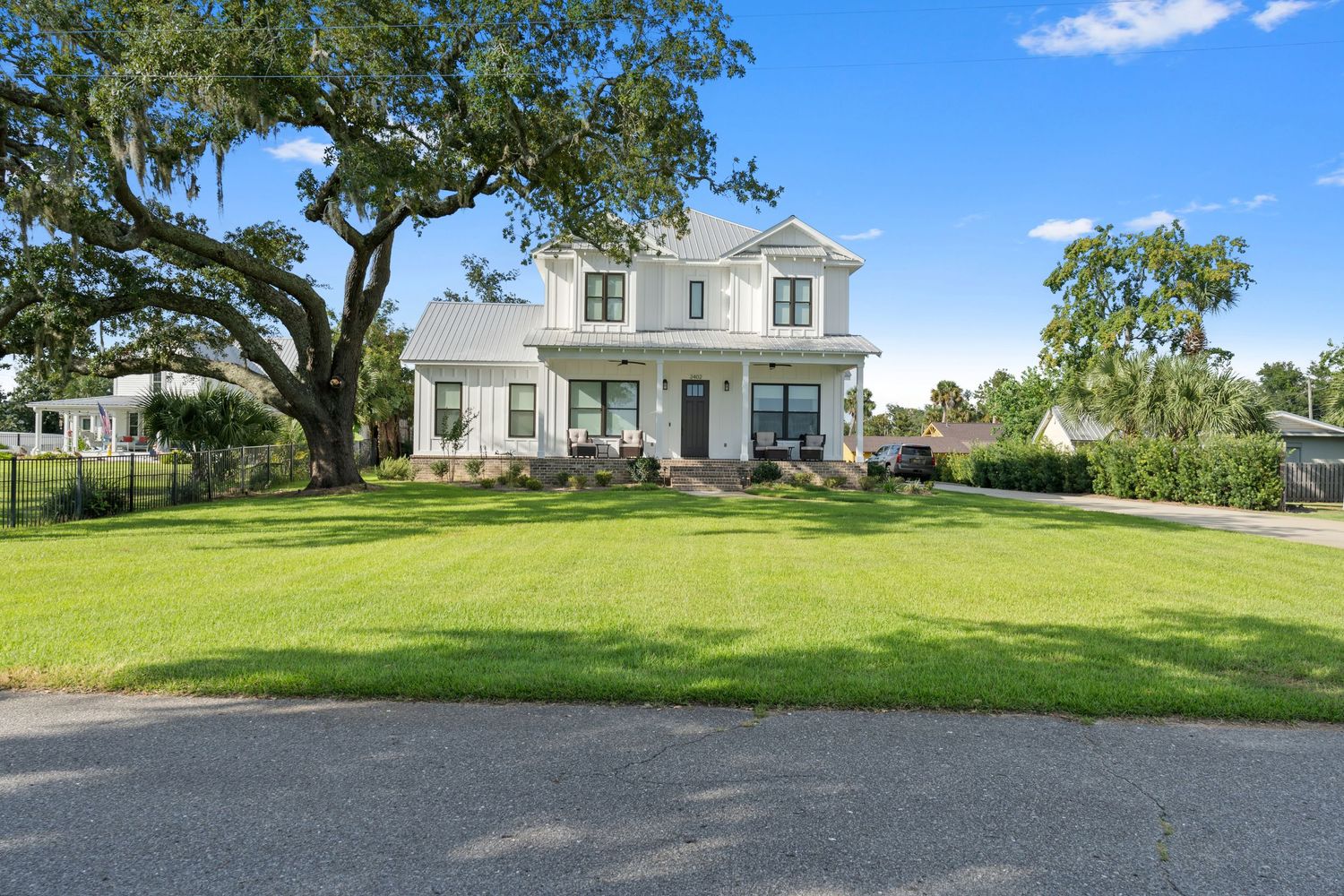 Two story home on the bay with green lawn and shady oak trees.