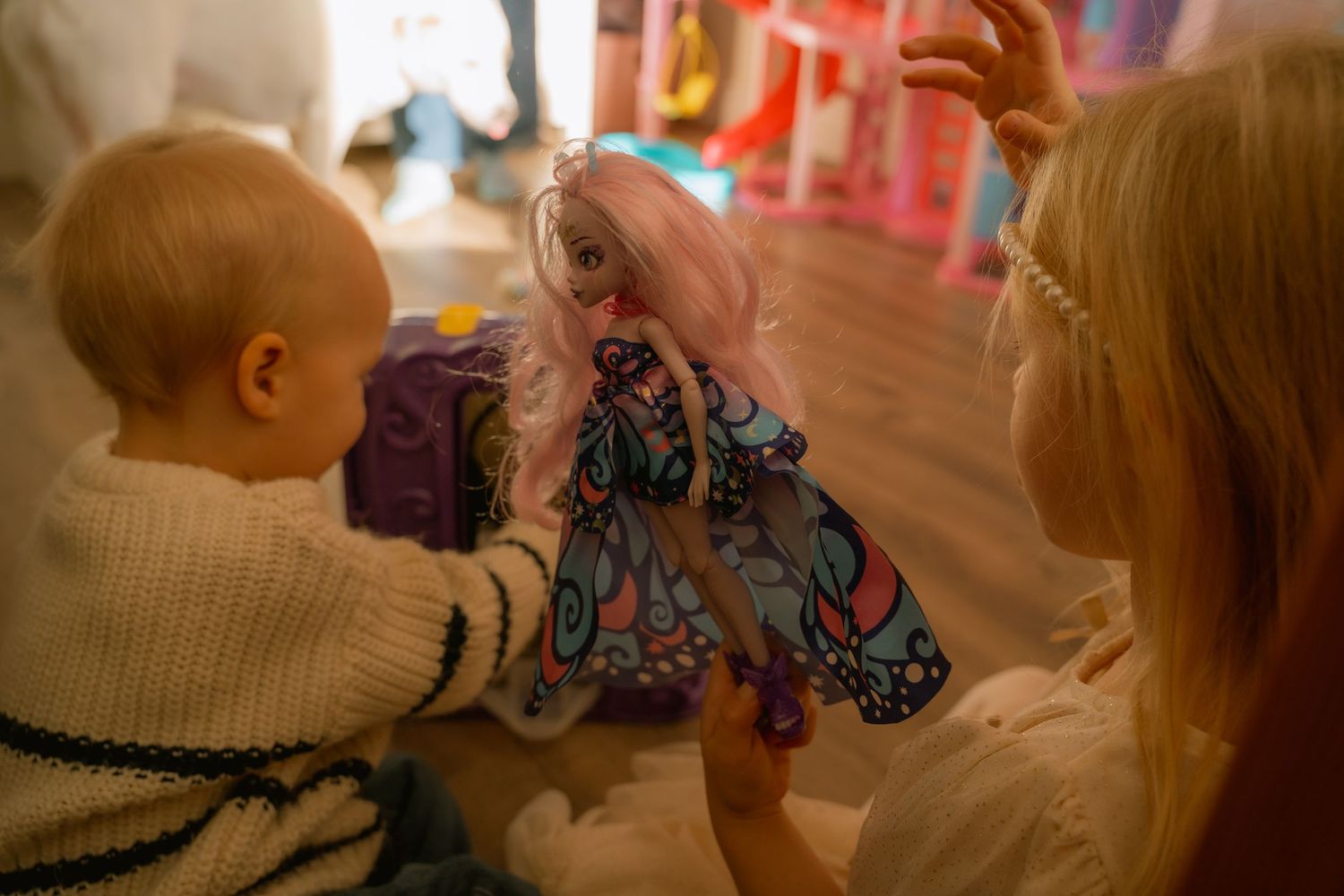 Candid in-home family photography in Hamilton — baby playing with a doll in a colorful playroom during everyday moments.