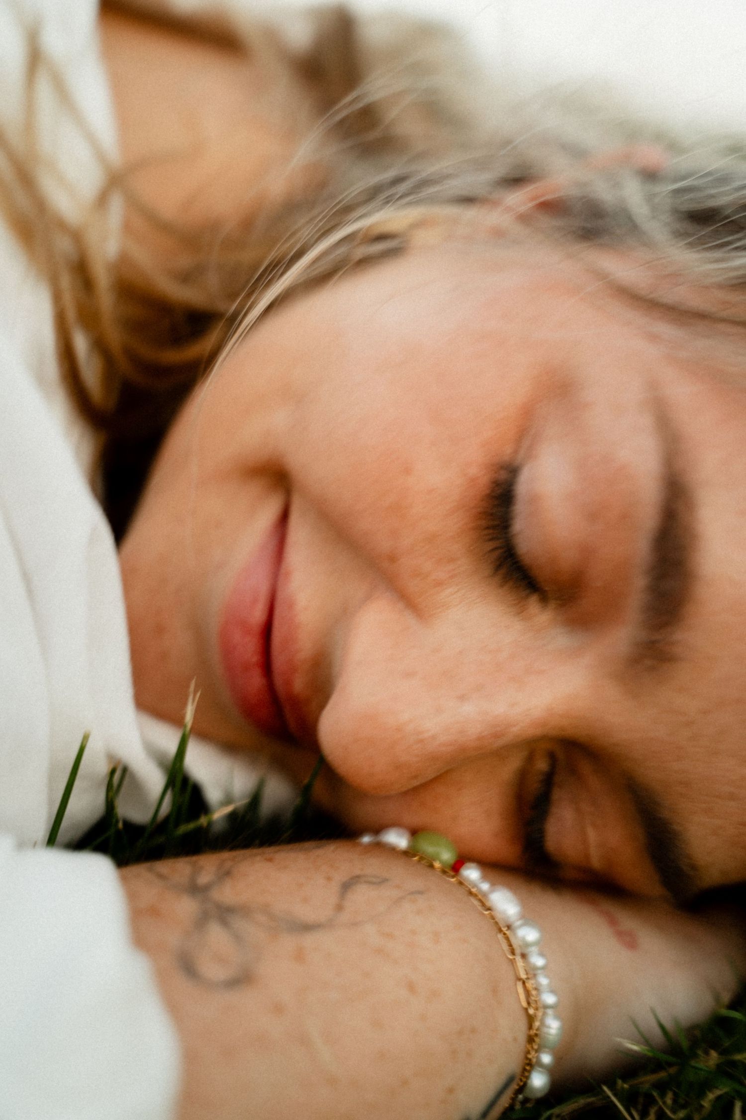 Close up shot of someone laying peacefully on grass with eyes closed and wearing a delicate pearl bracelet.