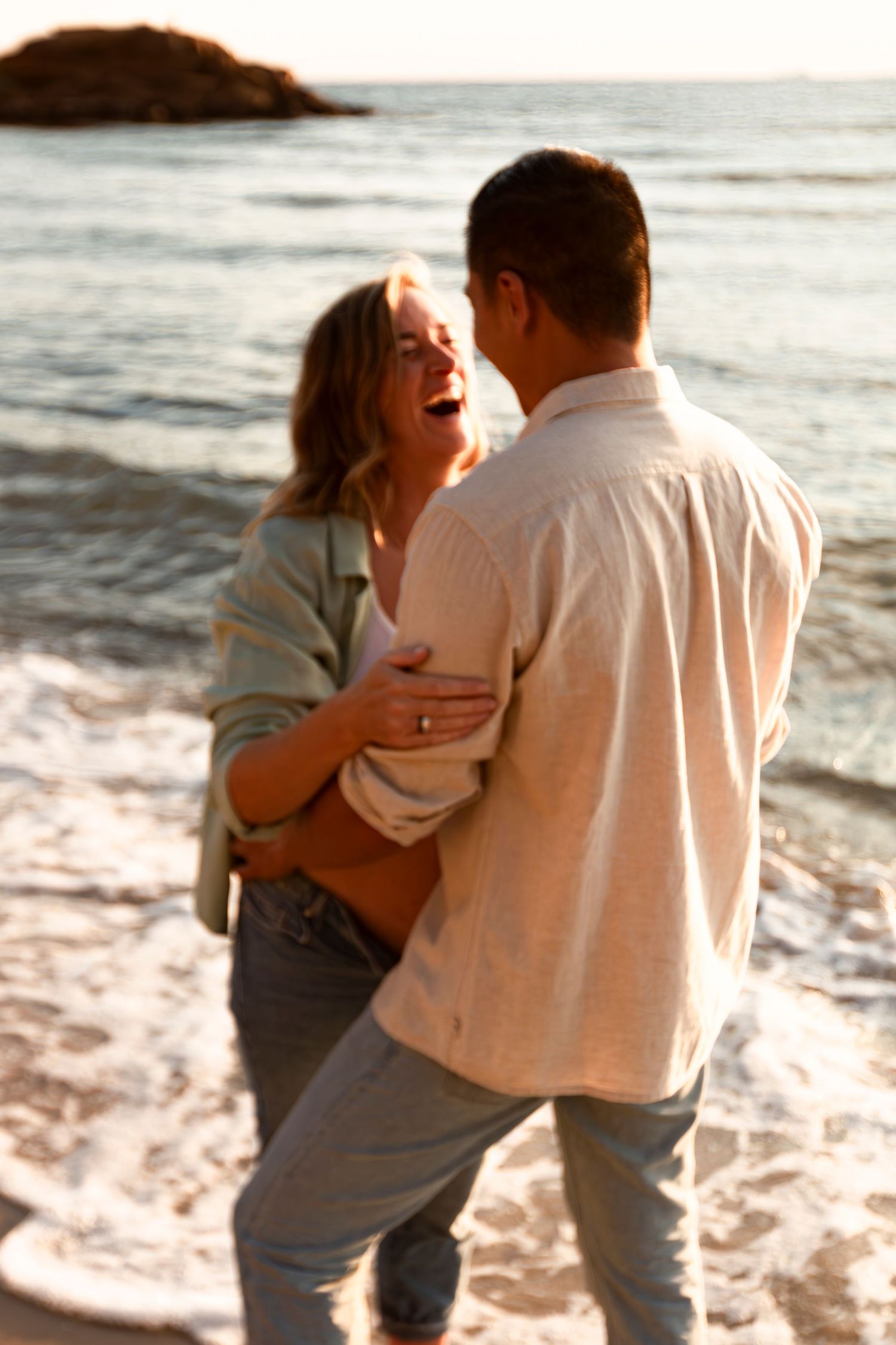 Couple sharing intimate moment on beach with ocean waves in background at sunset for their maternity session.