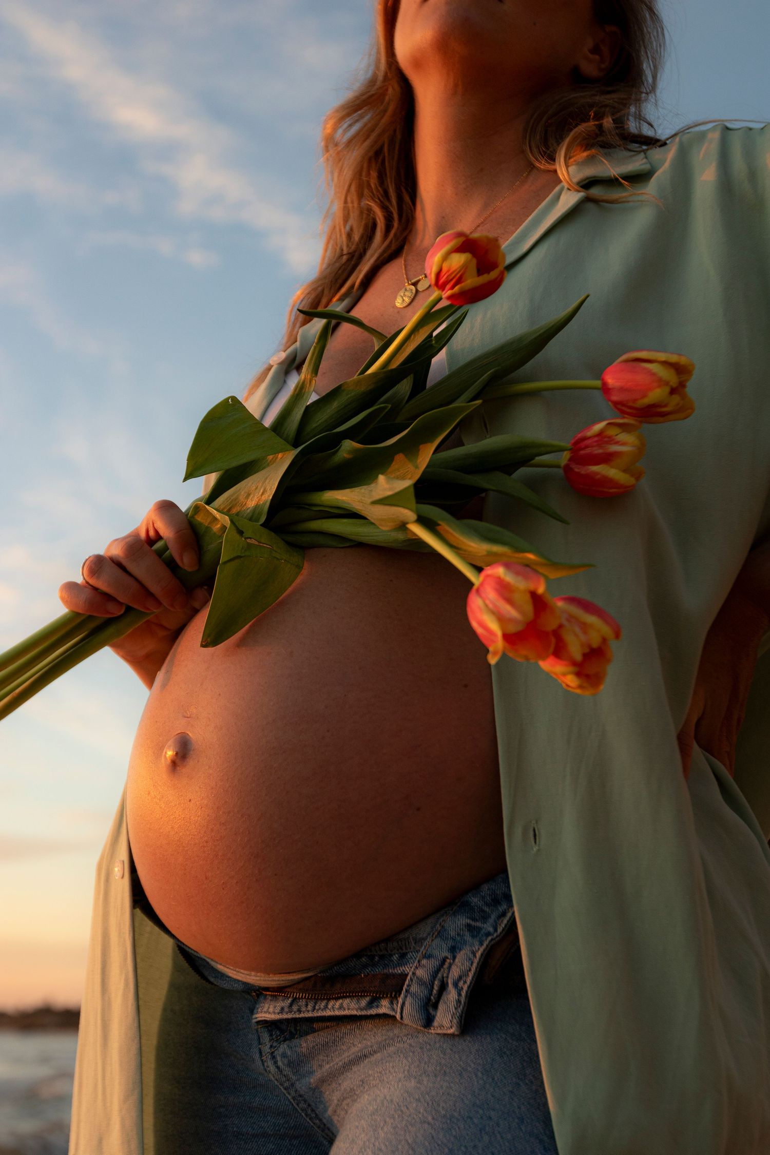 Artistic series of a pregnant belly with orange tulips at sunset creating a warm and intimate maternity photoshoot.