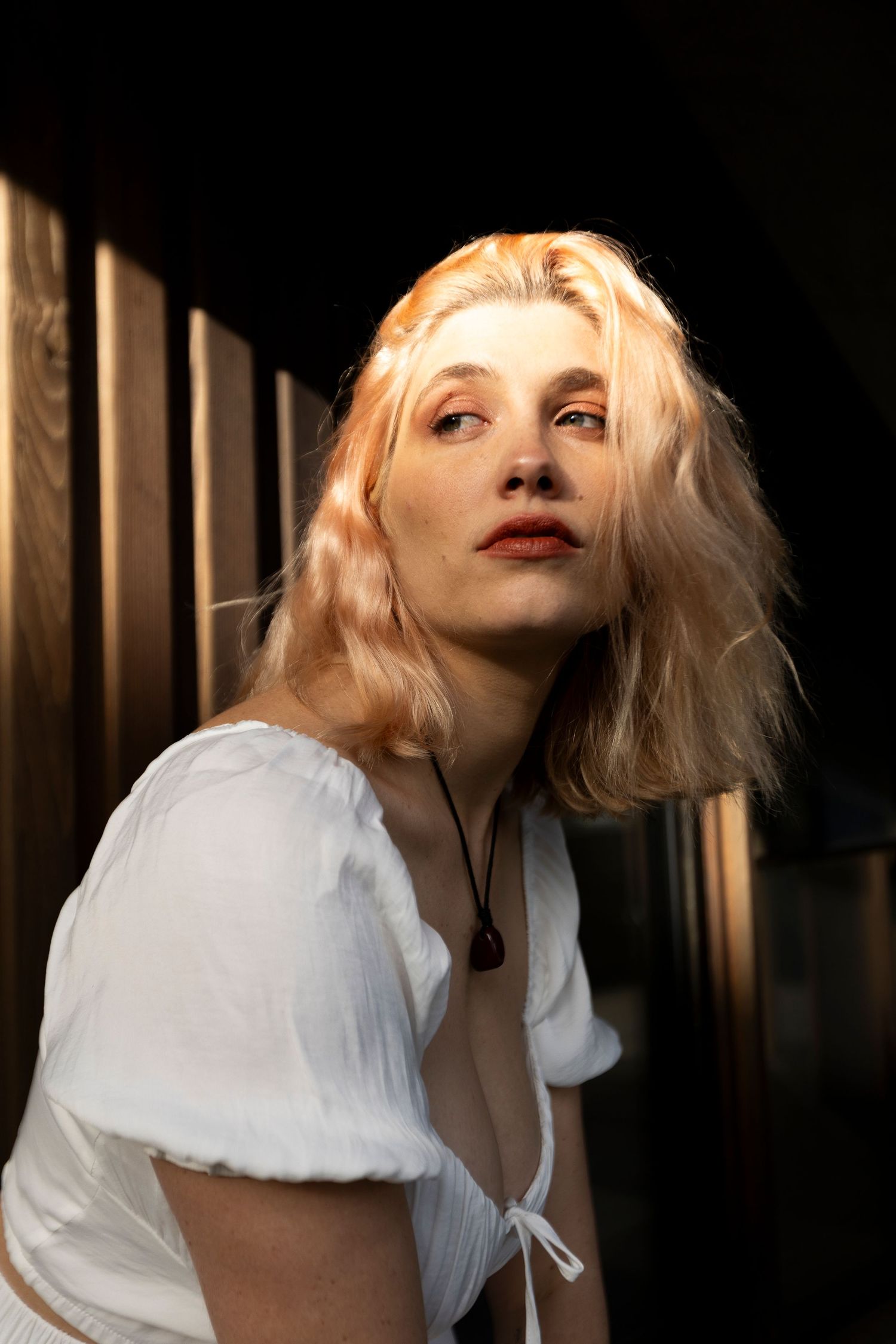 Dramatic portrait of a woman with blonde hair in white clothing against dark shadows.