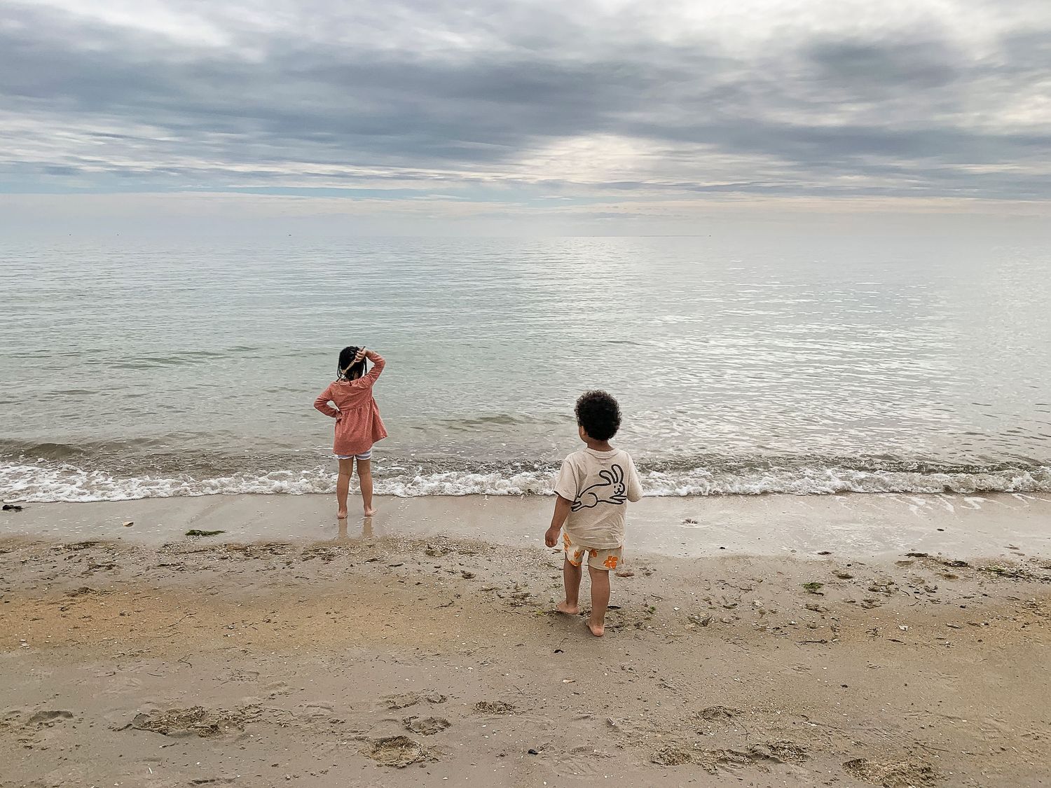 A series of beach photos showing people exploring the shoreline on a cloudy day at the water's edge.