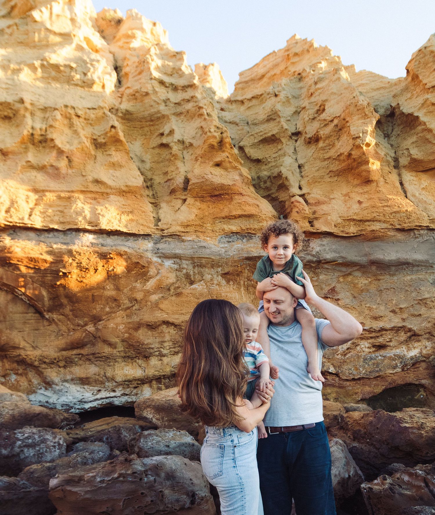 A family shares a tender moment against orange rocky cliffs at the beach.