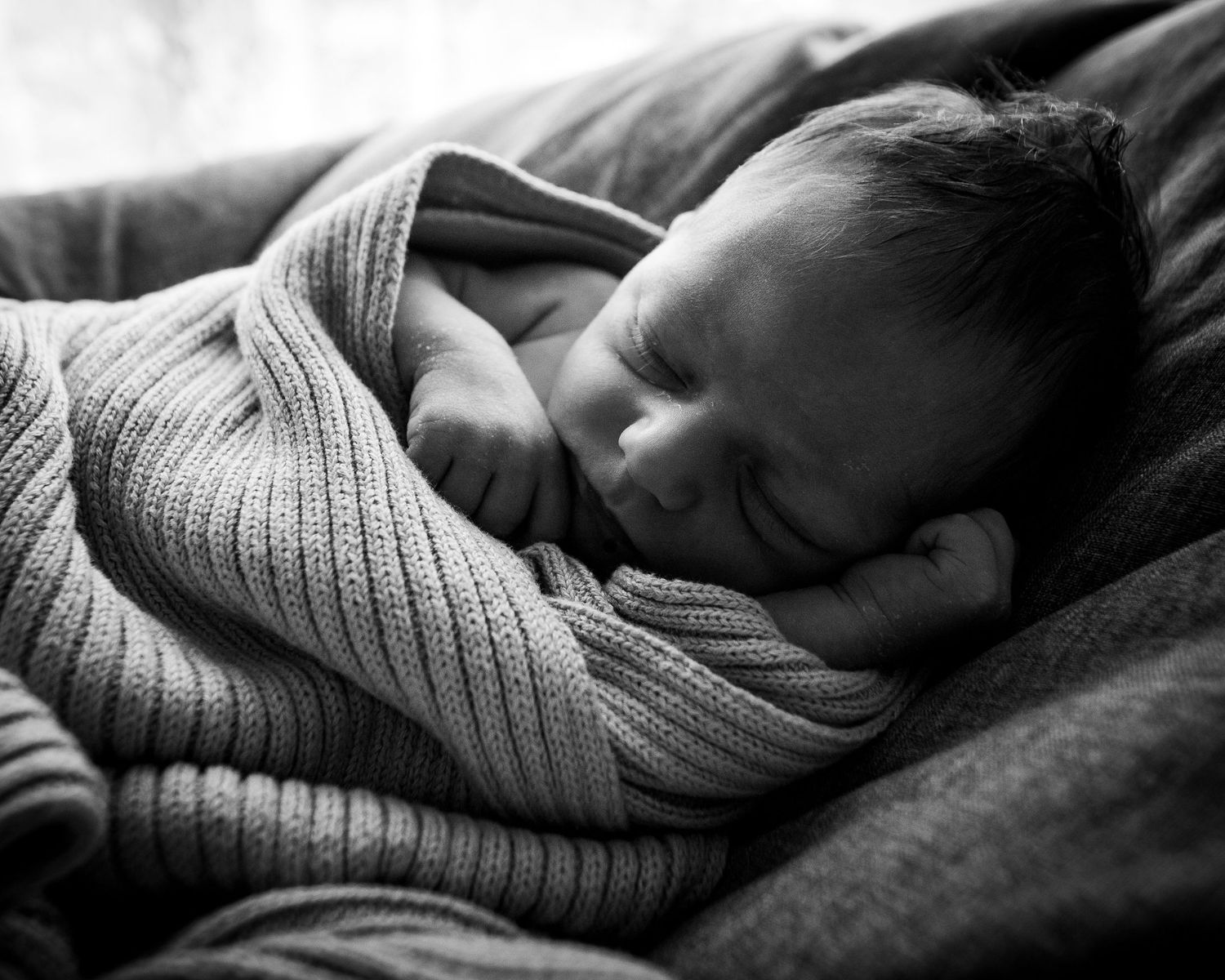 Peaceful black and white image of sleeping baby wrapped in knit blanket.