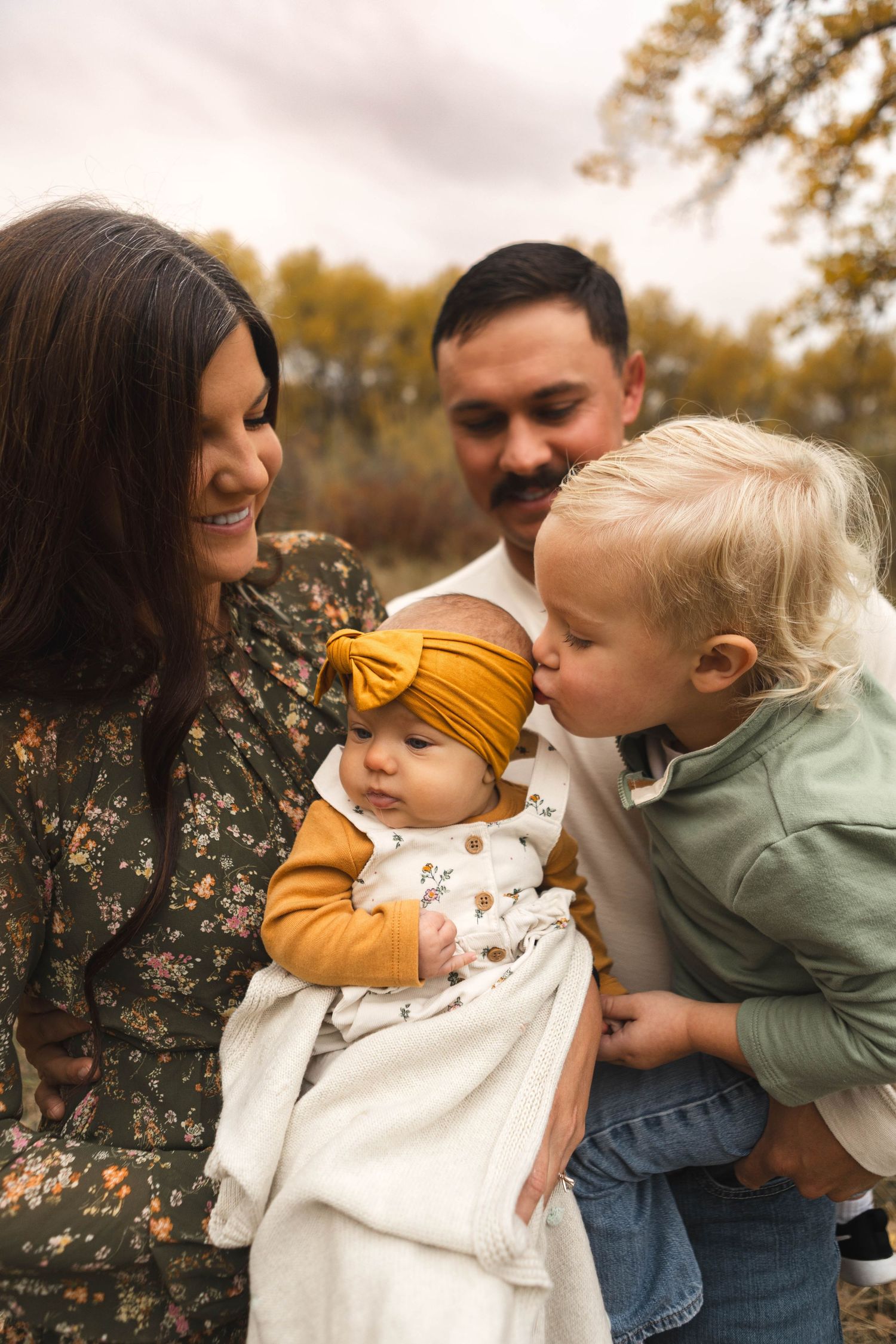 A family shares tender moments together during an outdoor autumn photoshoot with warm lighting and fall foliage.