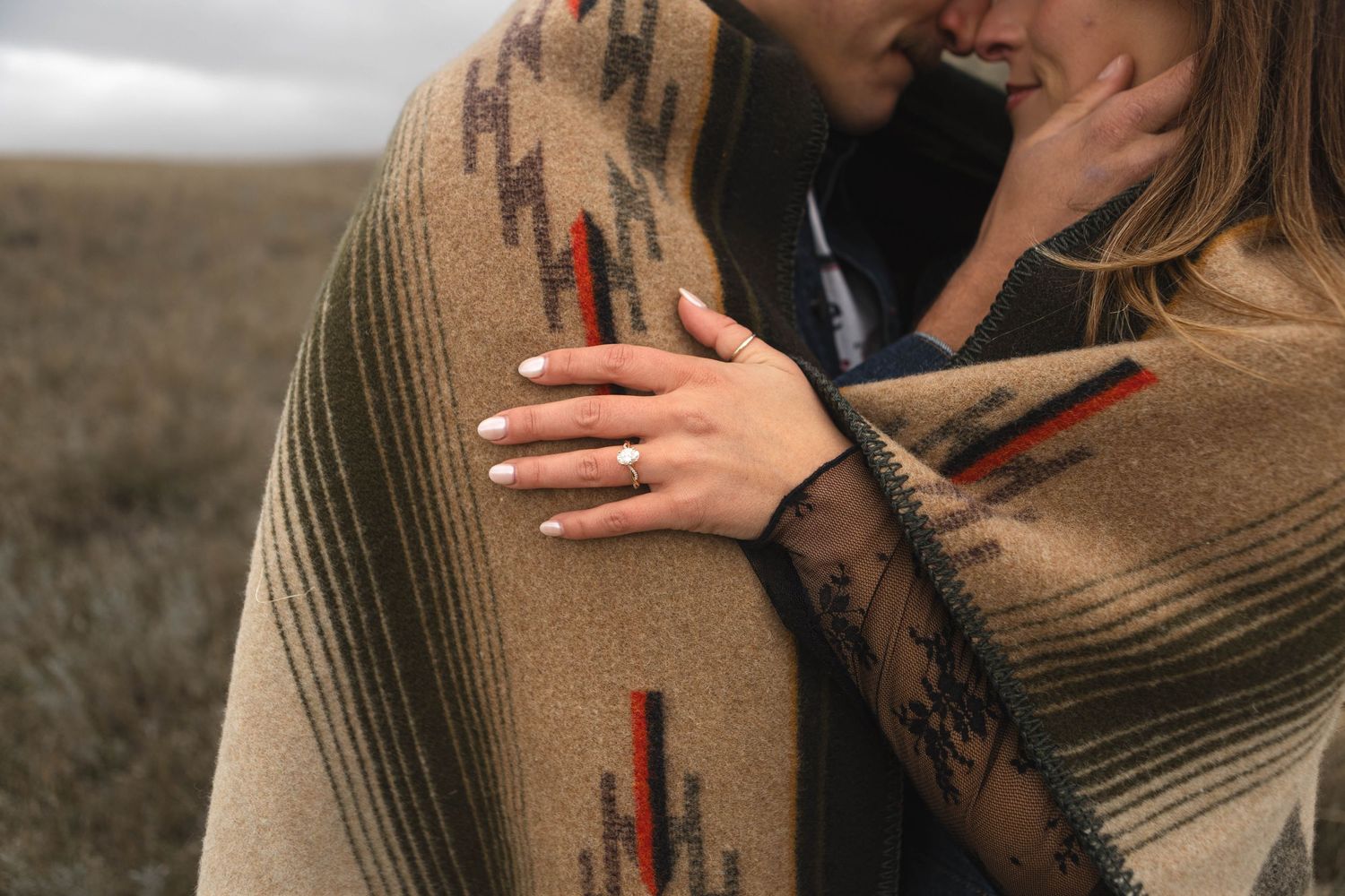 A couple in brown sweaters embrace tenderly in a romantic outdoor photoshoot at sunset.