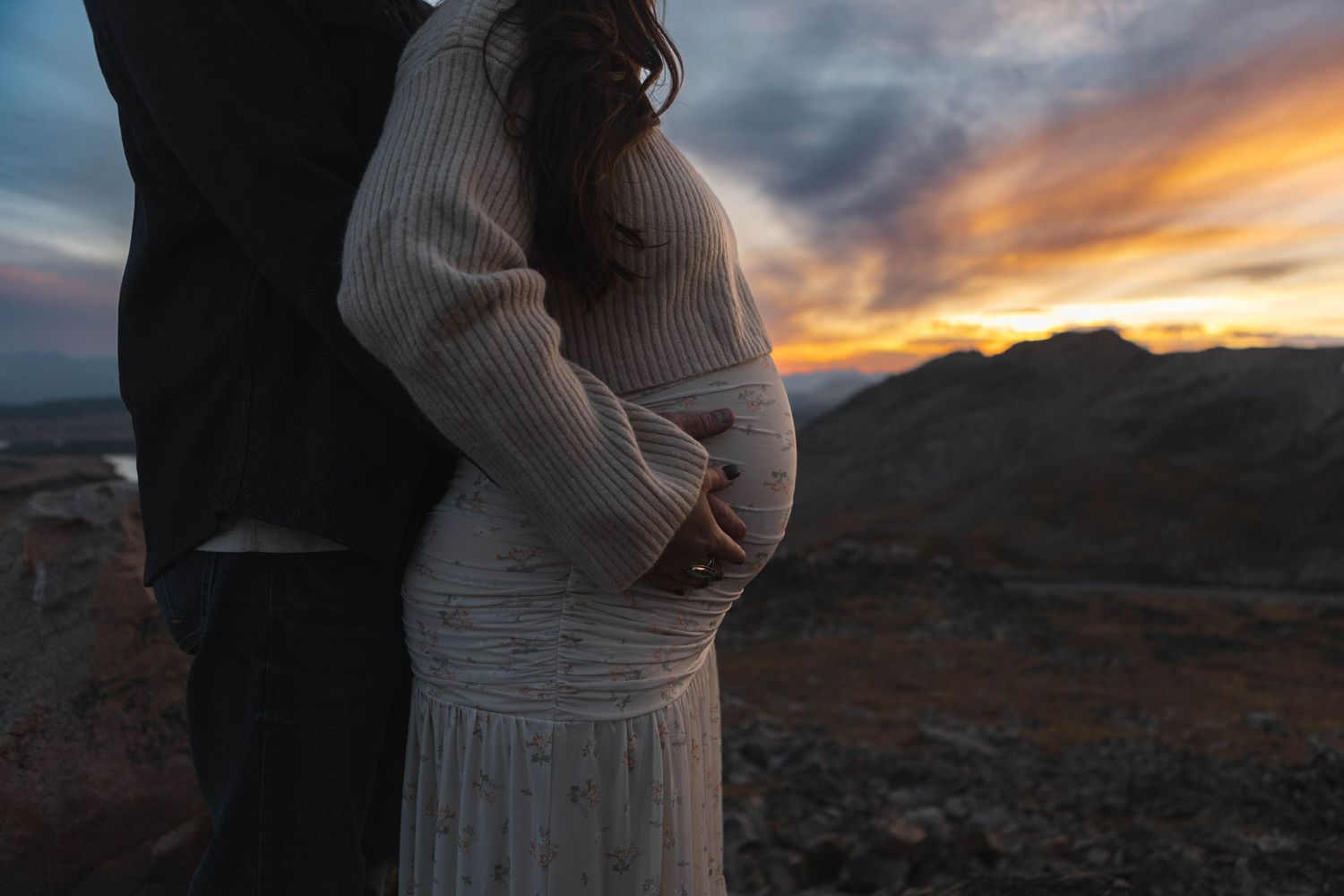 A couple embraces against a dramatic desert sunset with mountains silhouetted in the background.