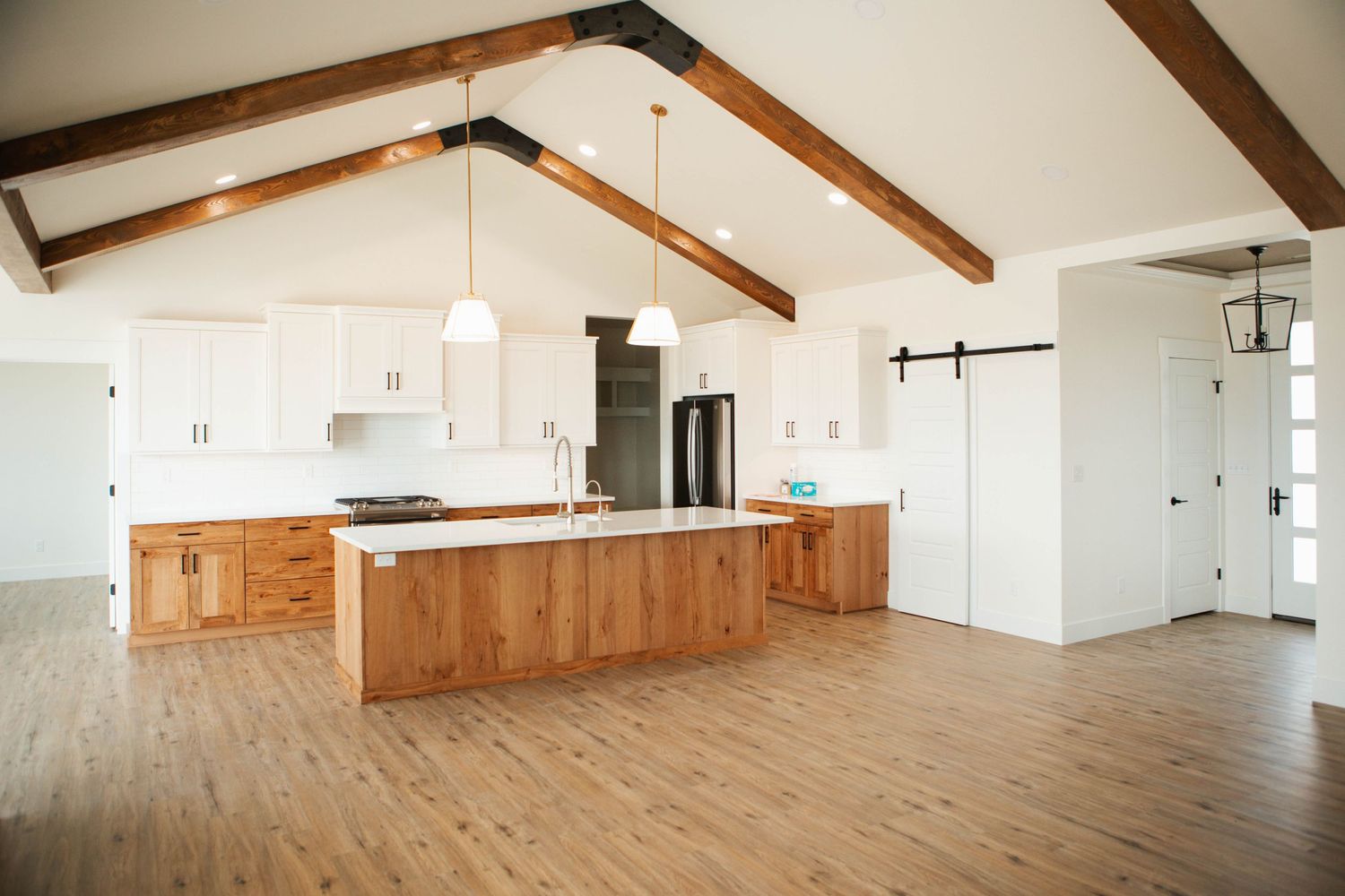 Modern open concept kitchen with vaulted ceiling, wood beams, white cabinets and large natural wood island.