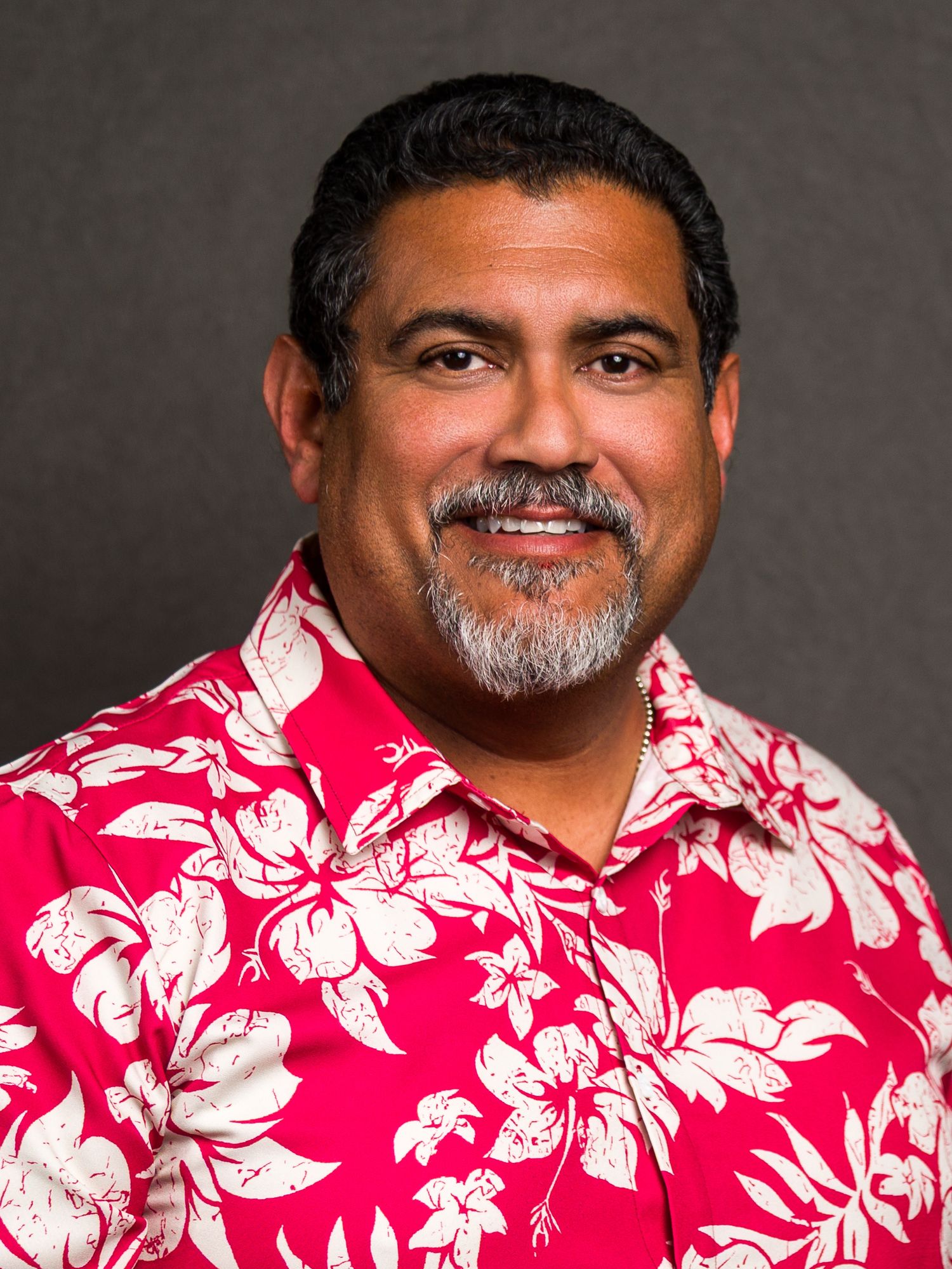 Person wearing a vibrant red and white Hawaiian floral print shirt against a dark gray background.