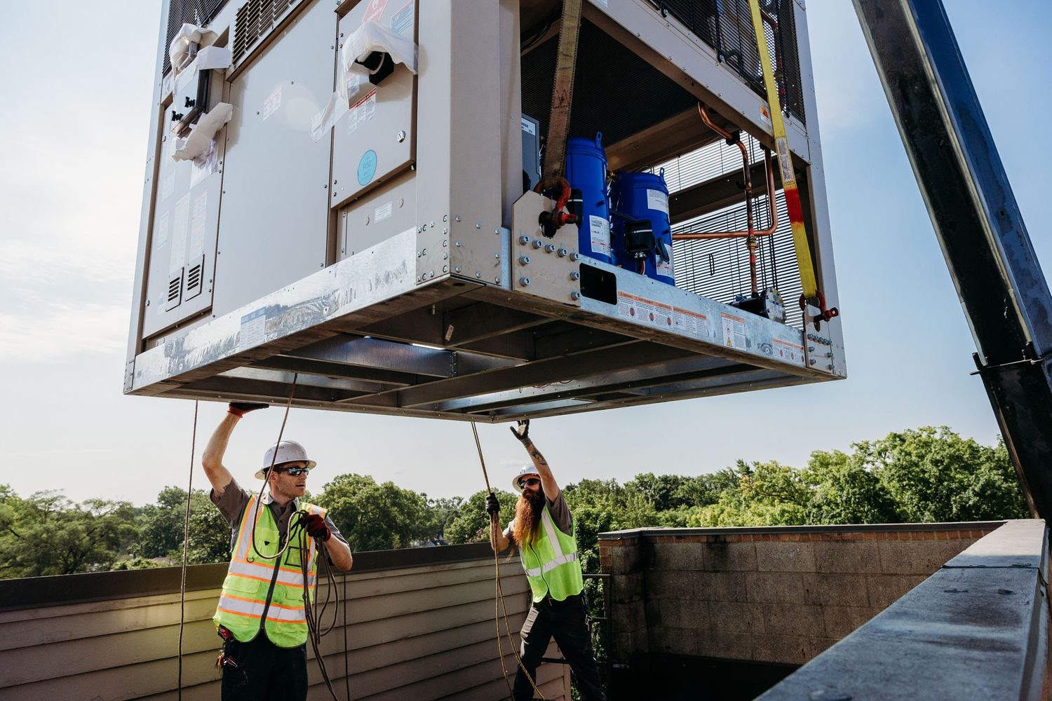 Construction workers in safety vests guide a large modular container unit being lowered by a crane.