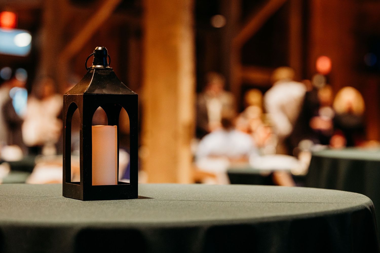 Black metal lantern with glowing candle centerpiece on draped table at elegant evening event.