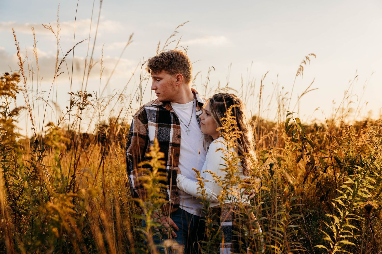 A person stands in a golden field of tall grass and wildflowers during sunset with warm autumn light.
