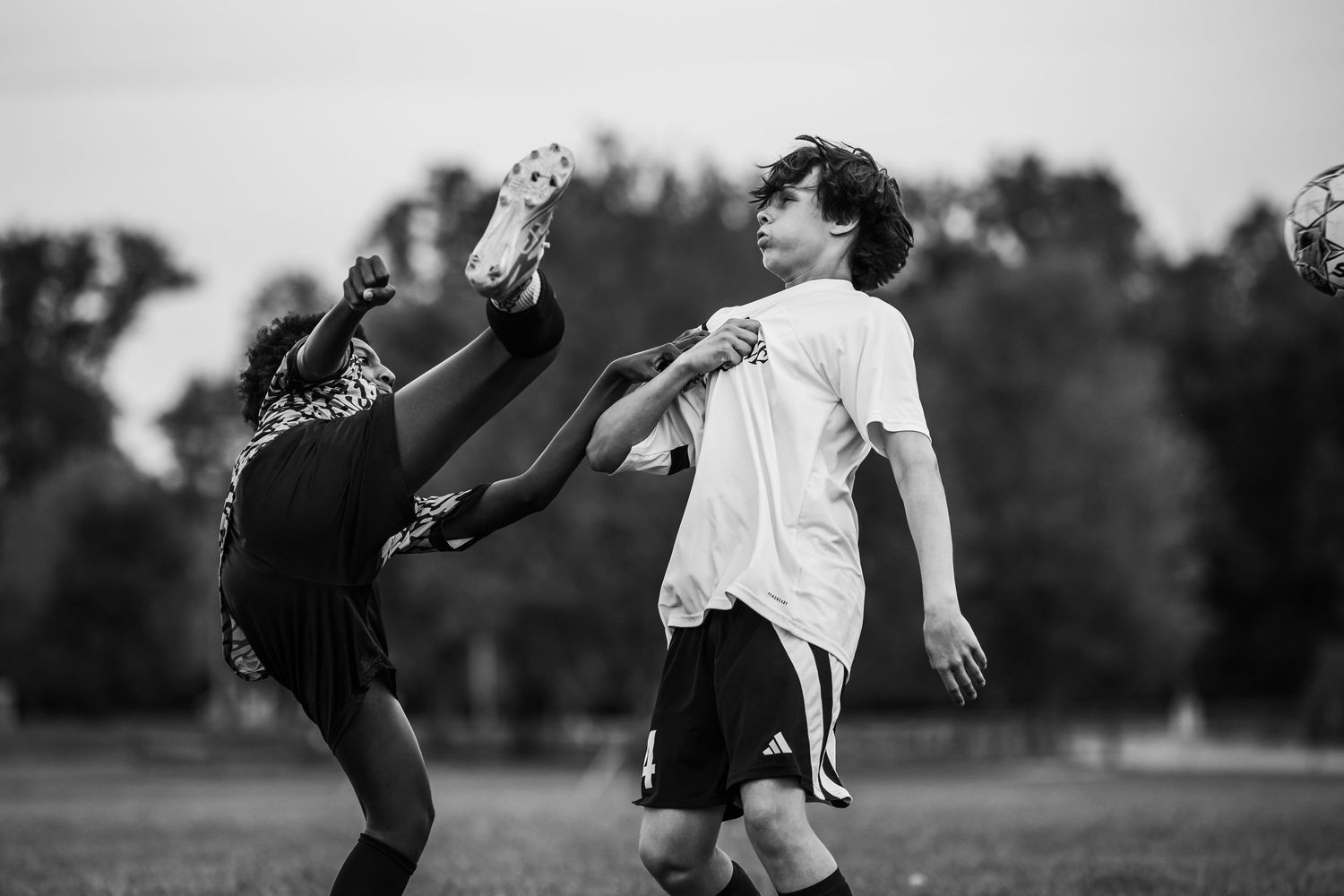 Two youth soccer players compete for the ball in an intense black and white action shot on a grass field.