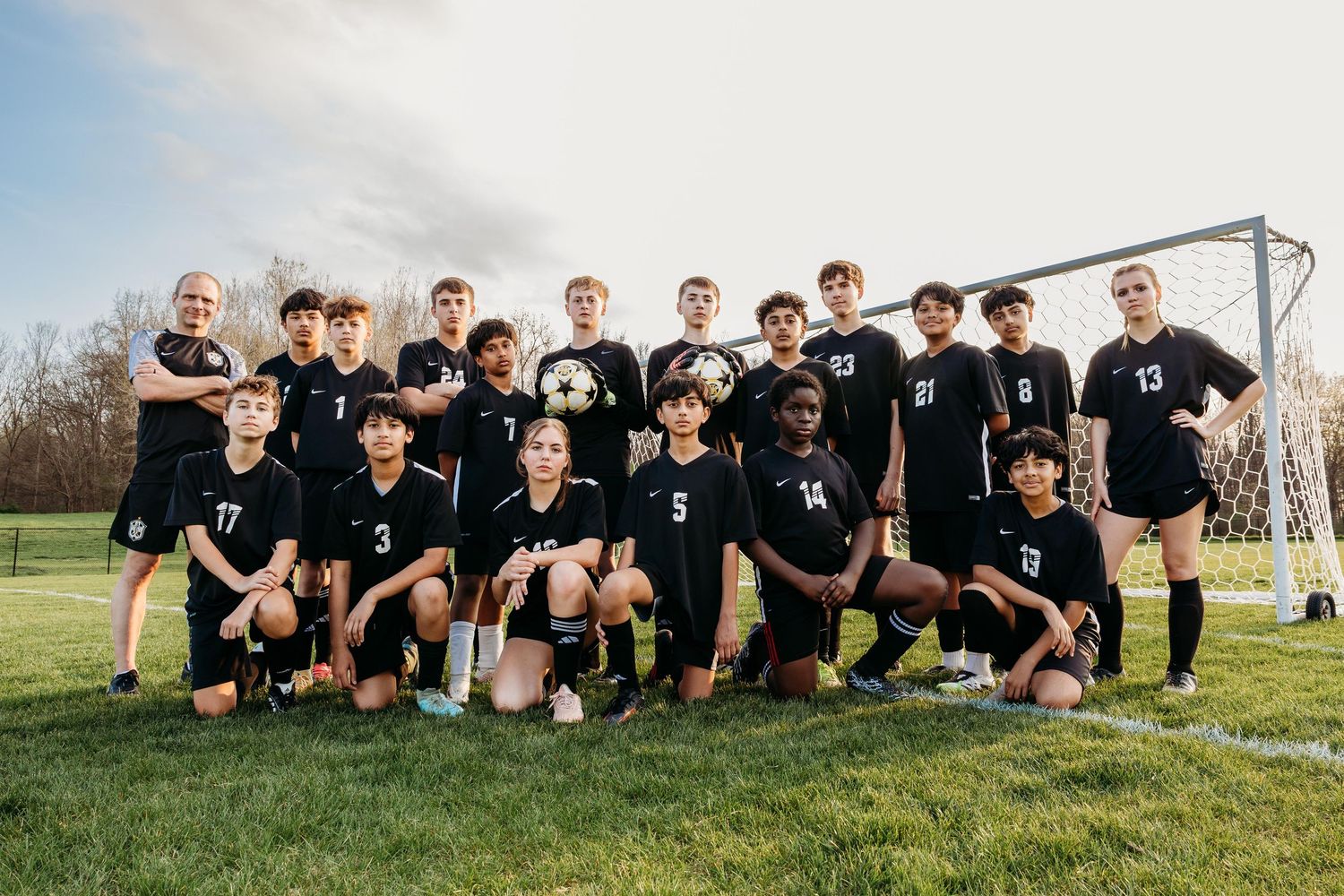 Boys soccer team in black uniforms posing together on a grass field in front of a goal post.