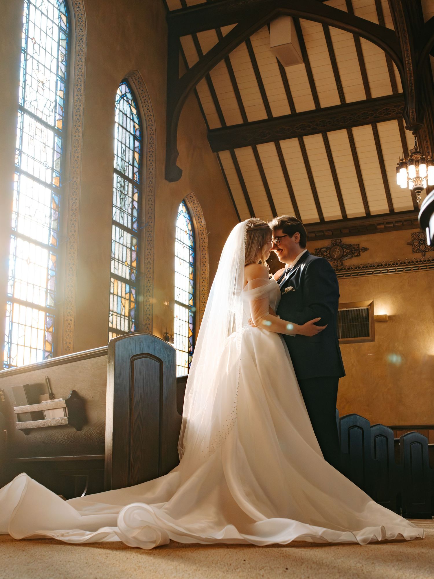 Romantic wedding couple shares intimate moments in a sunlit church with stained glass windows and dramatic cathedral ceilings.