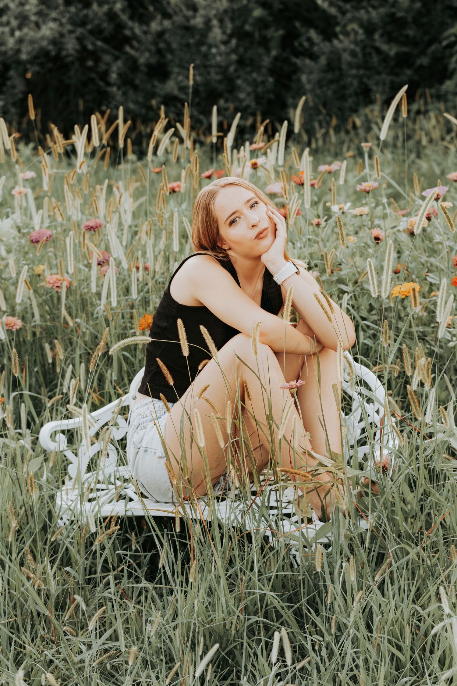 A person lying in a dreamy summer meadow surrounded by tall grasses and wildflowers during golden hour.