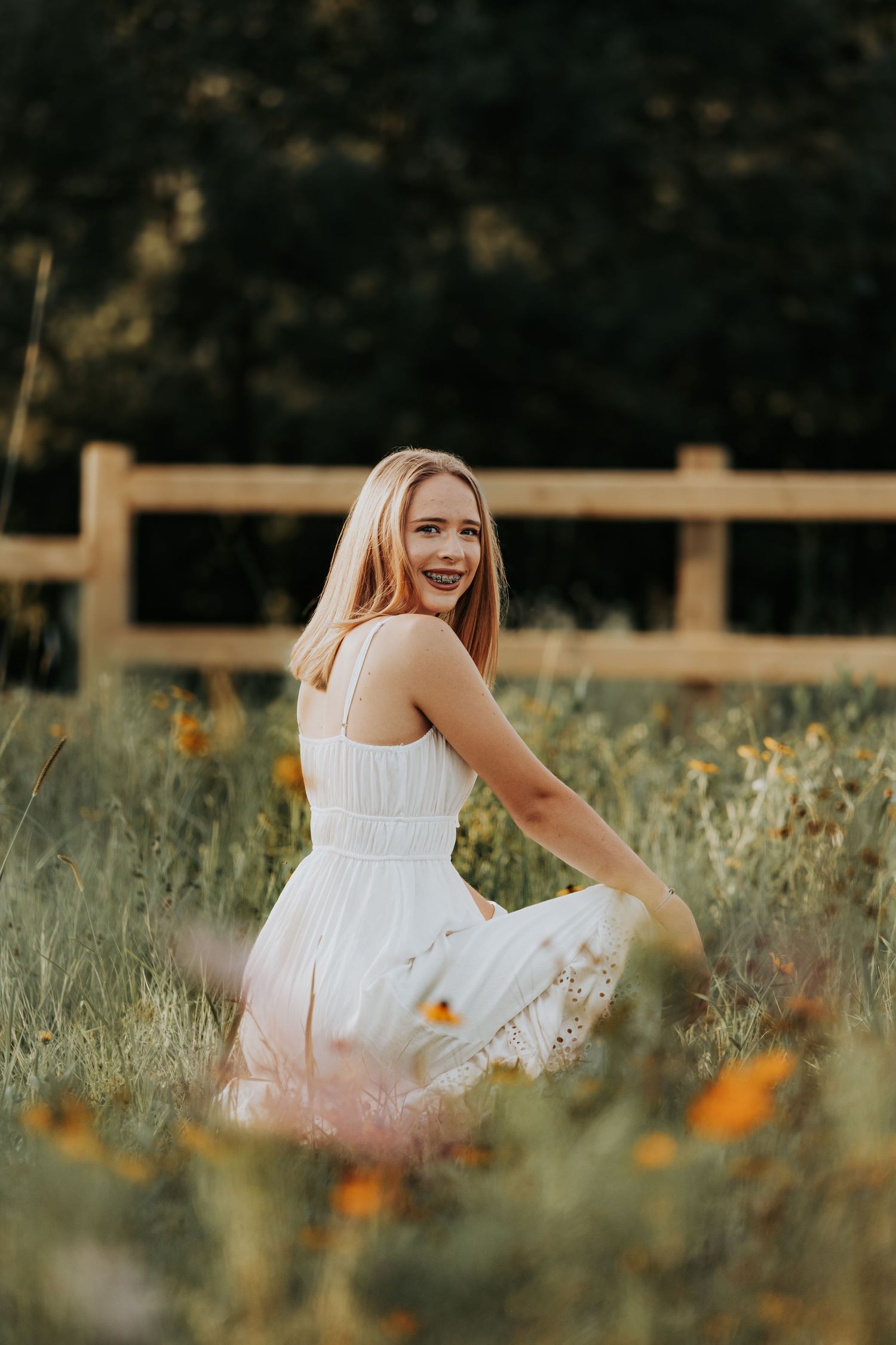 A person wearing a white dress sits gracefully among wildflowers in a field at sunset.