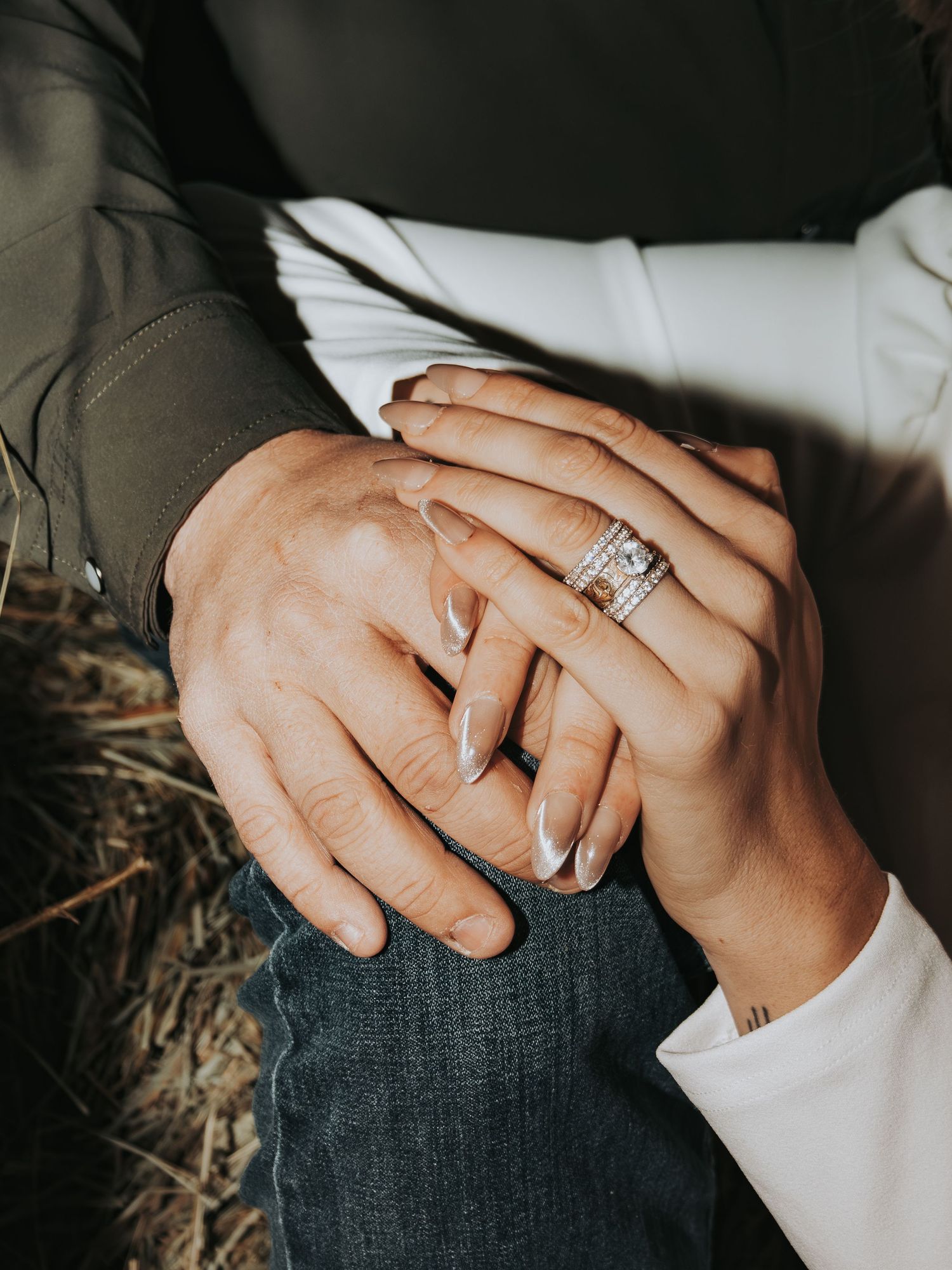 Close-up of hands with engagement ring showing intimate moment between couple on denim and camouflage clothing.