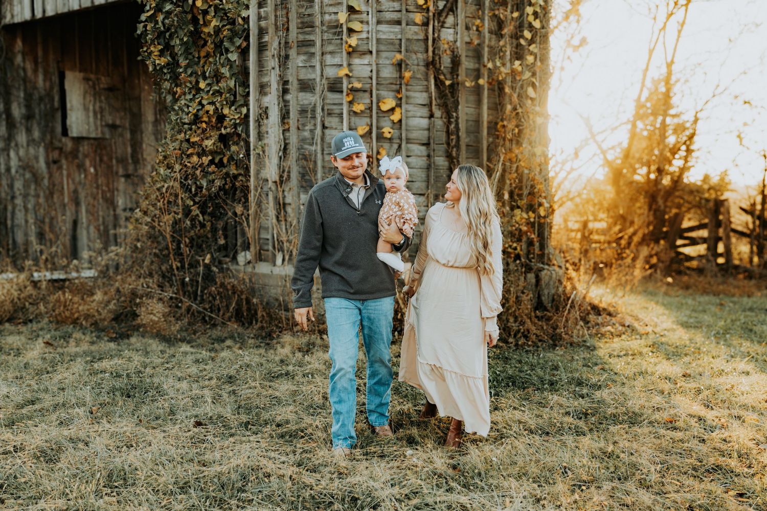 A romantic couple embraces near a rustic wooden barn during a golden sunset photo session.