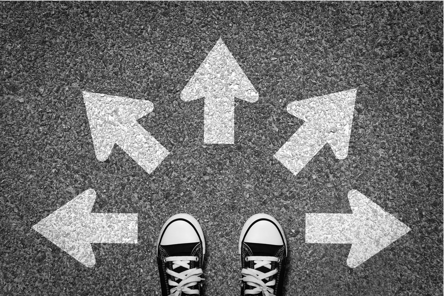 Black and white city street with person's feet in front of several arrows signaling which direction they should go.