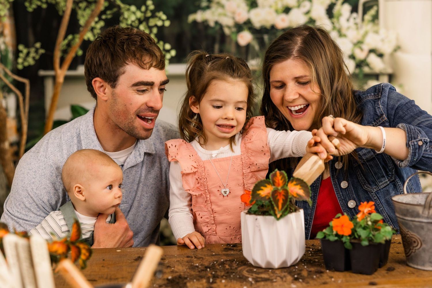 Family of four enjoying gardening together, planting colorful flowers in a white pot on a wooden table.