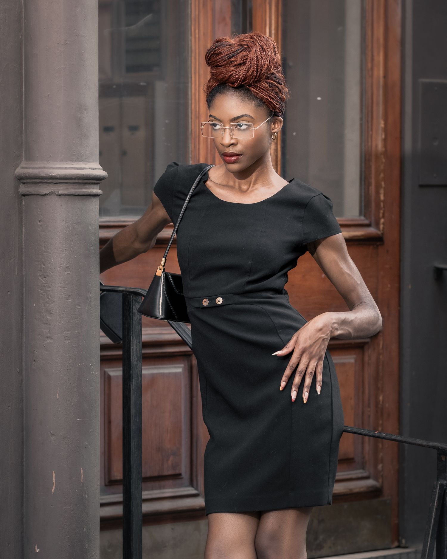 Editorial fashion photography: model in black dress with copper hair bun posing on vintage wooden stairs, urban lifestyle aesthetic.