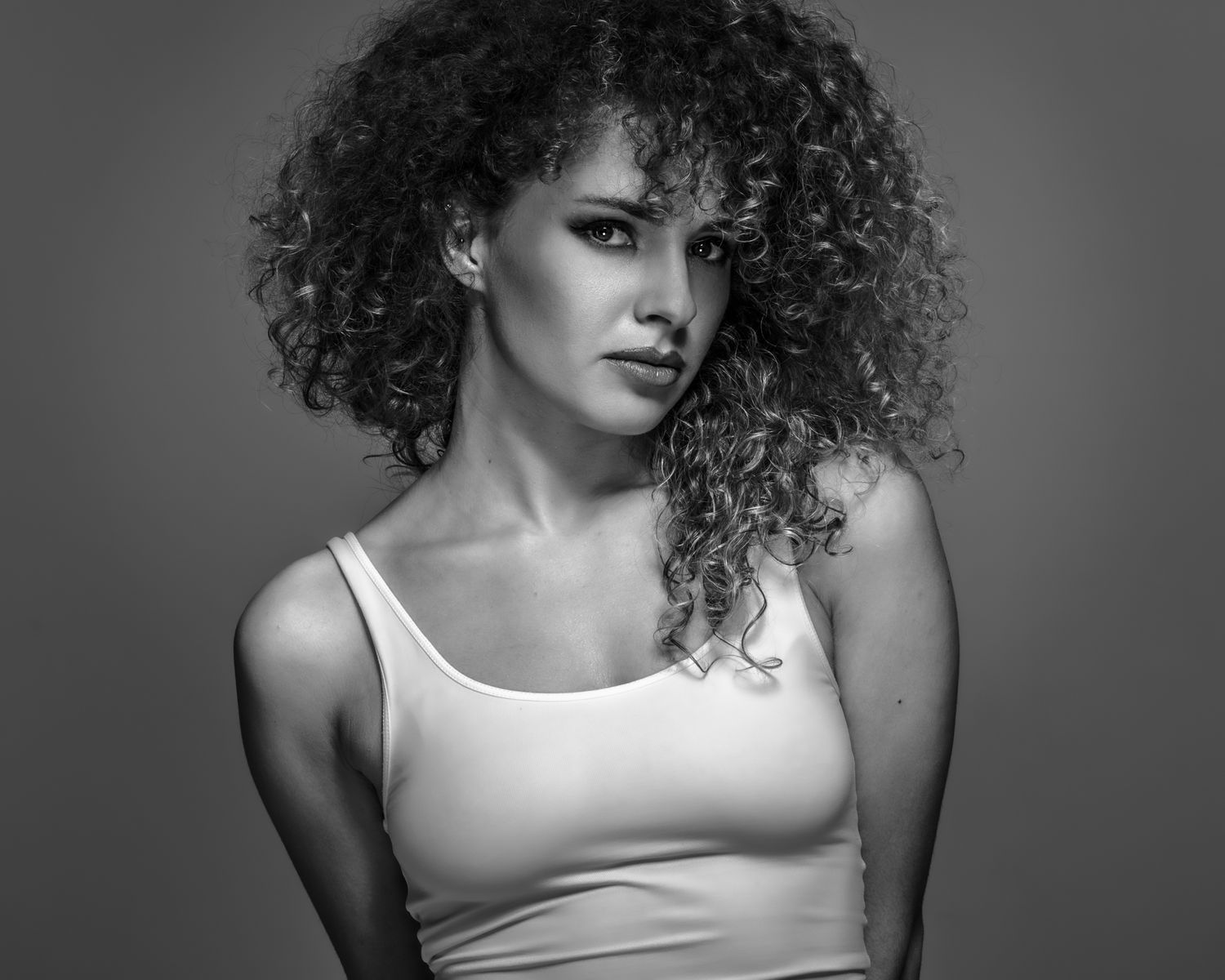 Classic black and white beauty portrait of a model with large curly hair, white tank top, neutral background, global portfolio.