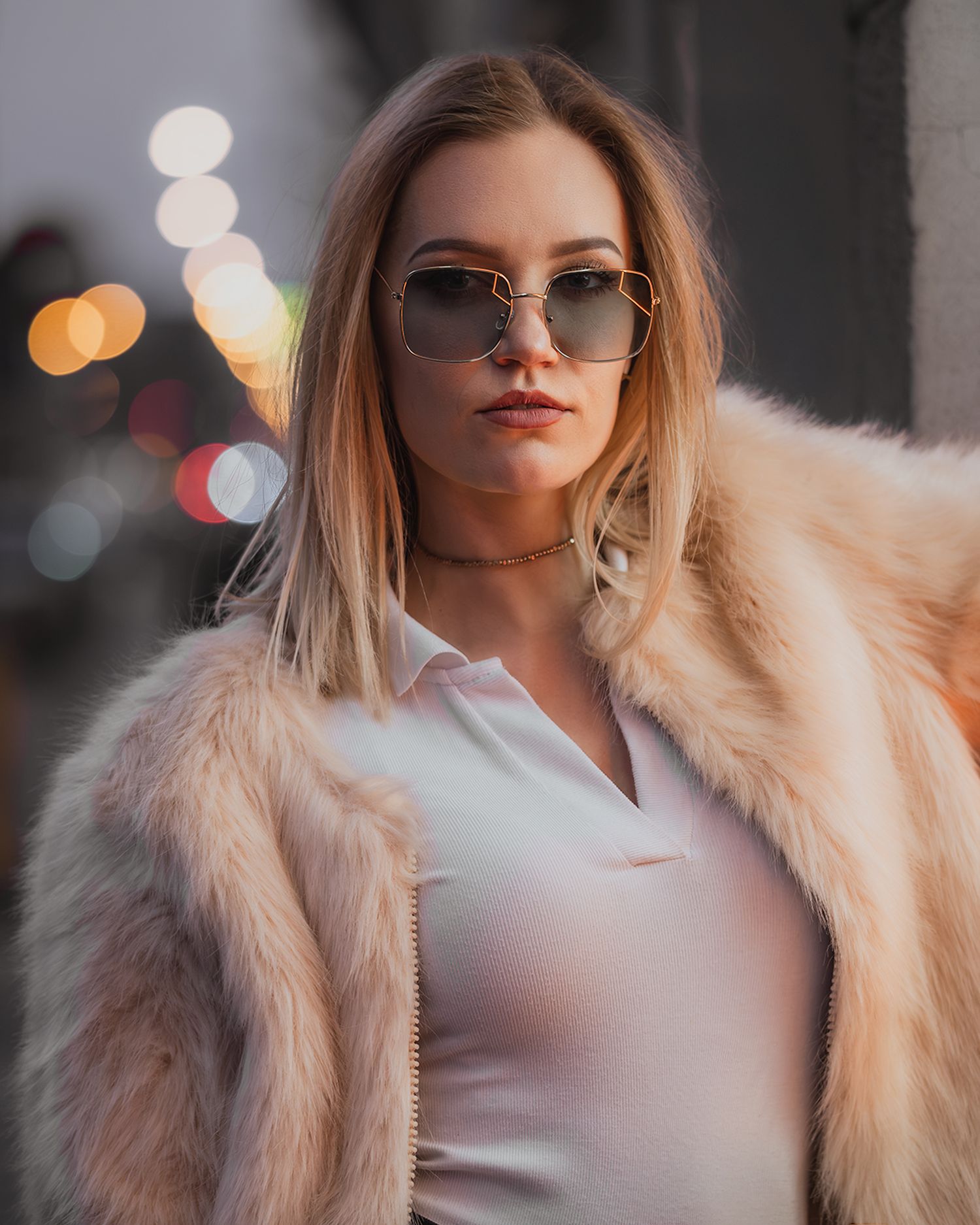 Urban glamour fashion: portrait of model in pink faux fur coat & squared sunglasses, street background with bokeh, global portfolio.