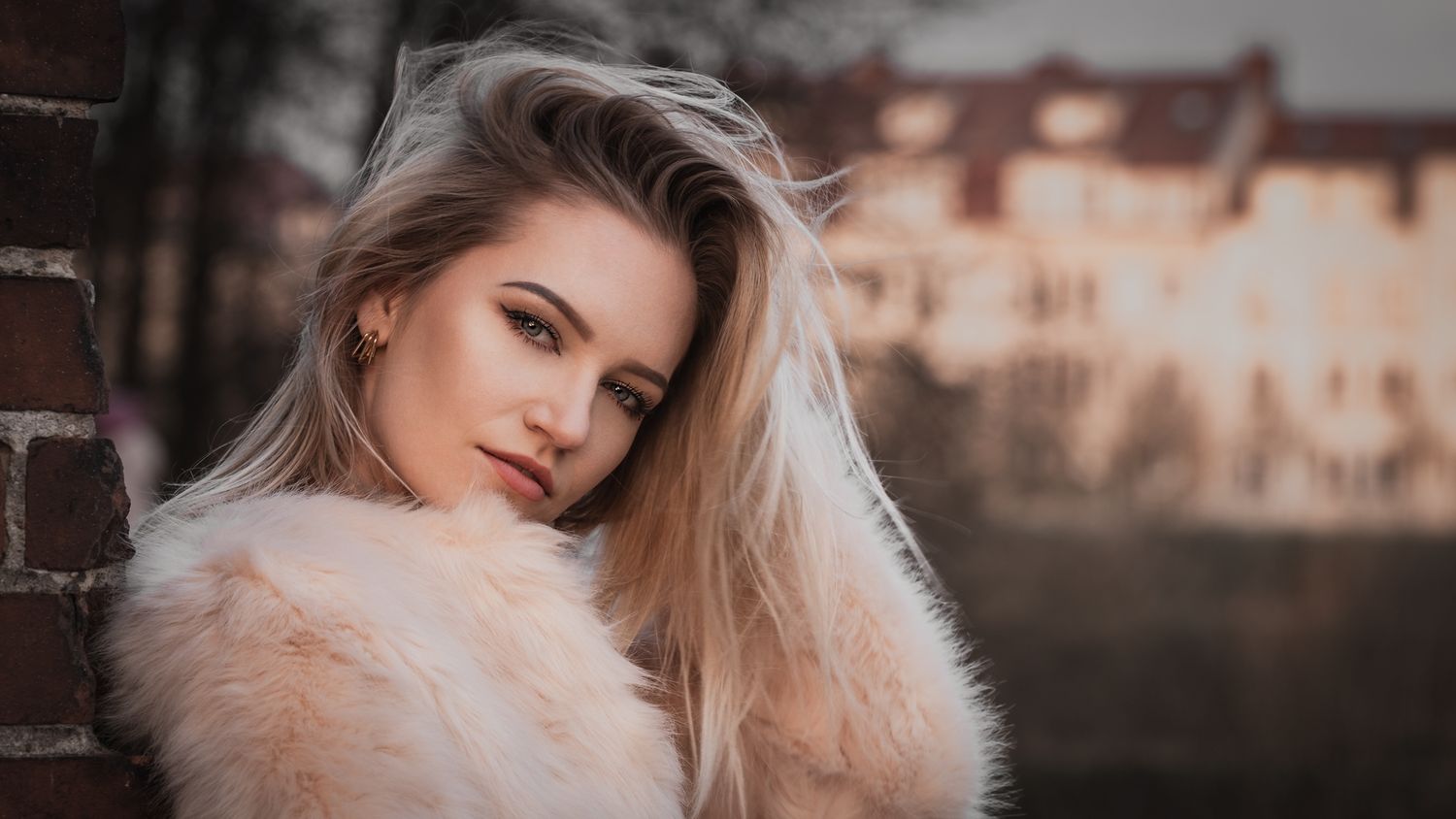 Profile fashion portrait: model in pink faux fur jacket, dramatic sunset light on face, blurred city background, global portfolio shot.
