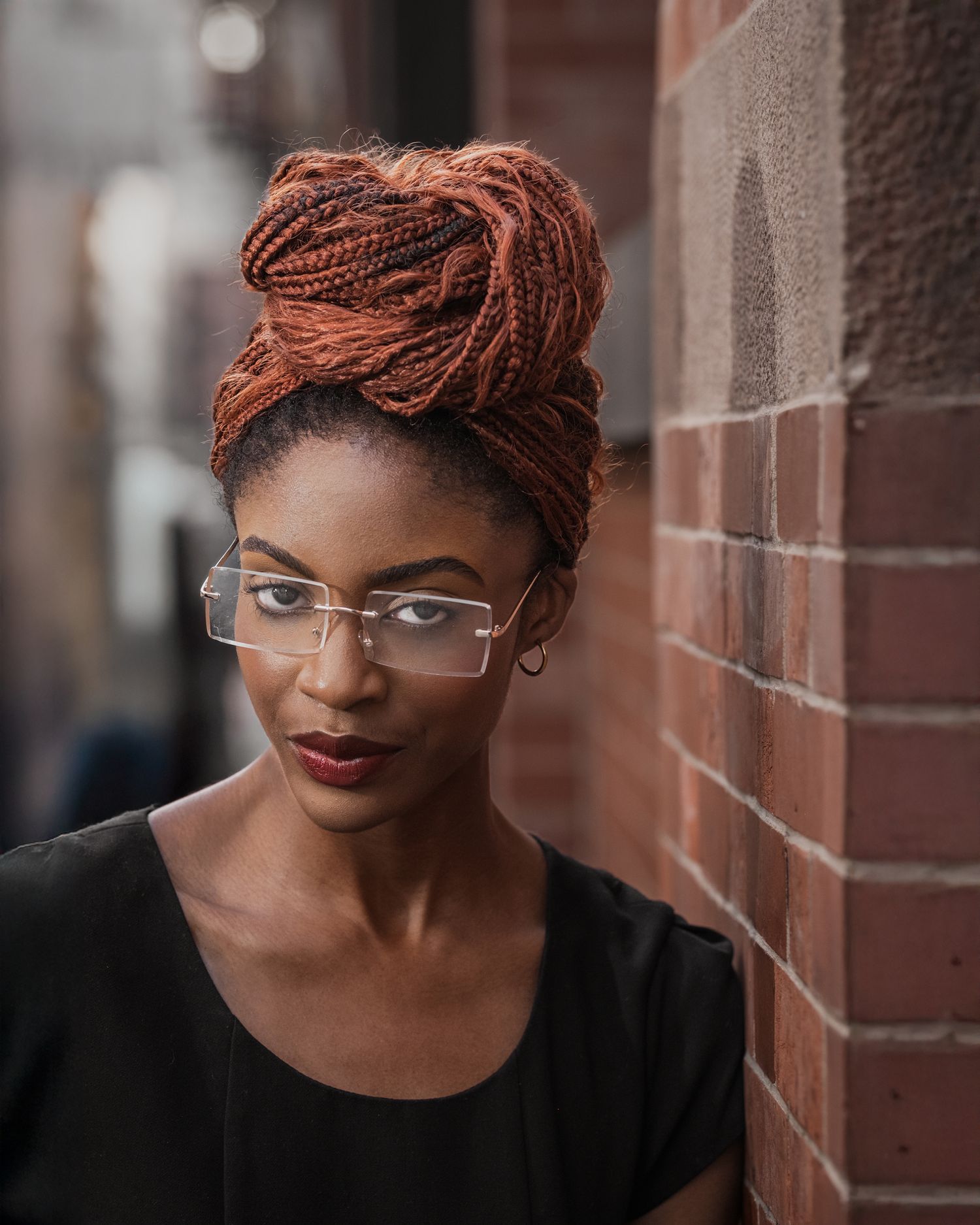 Detailed fashion portrait: close-up on model with intricate copper bun, clear optical glasses, moody professional studio lighting.