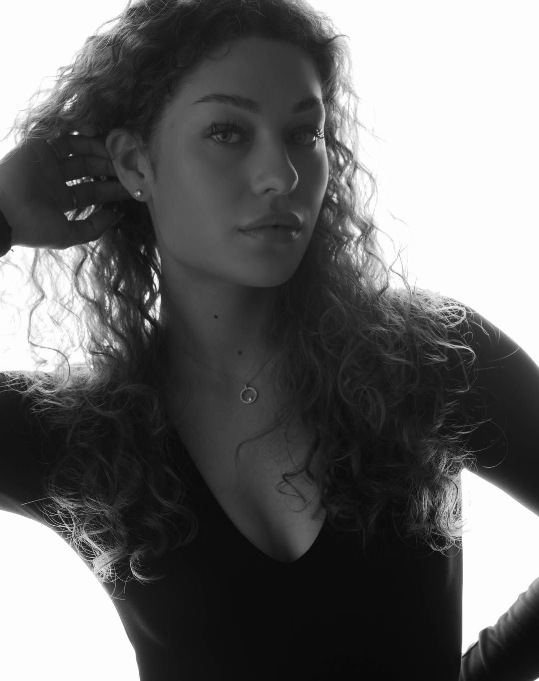 Black and white portrait of a young woman with curly hair wearing a v-neck top and delicate necklace.