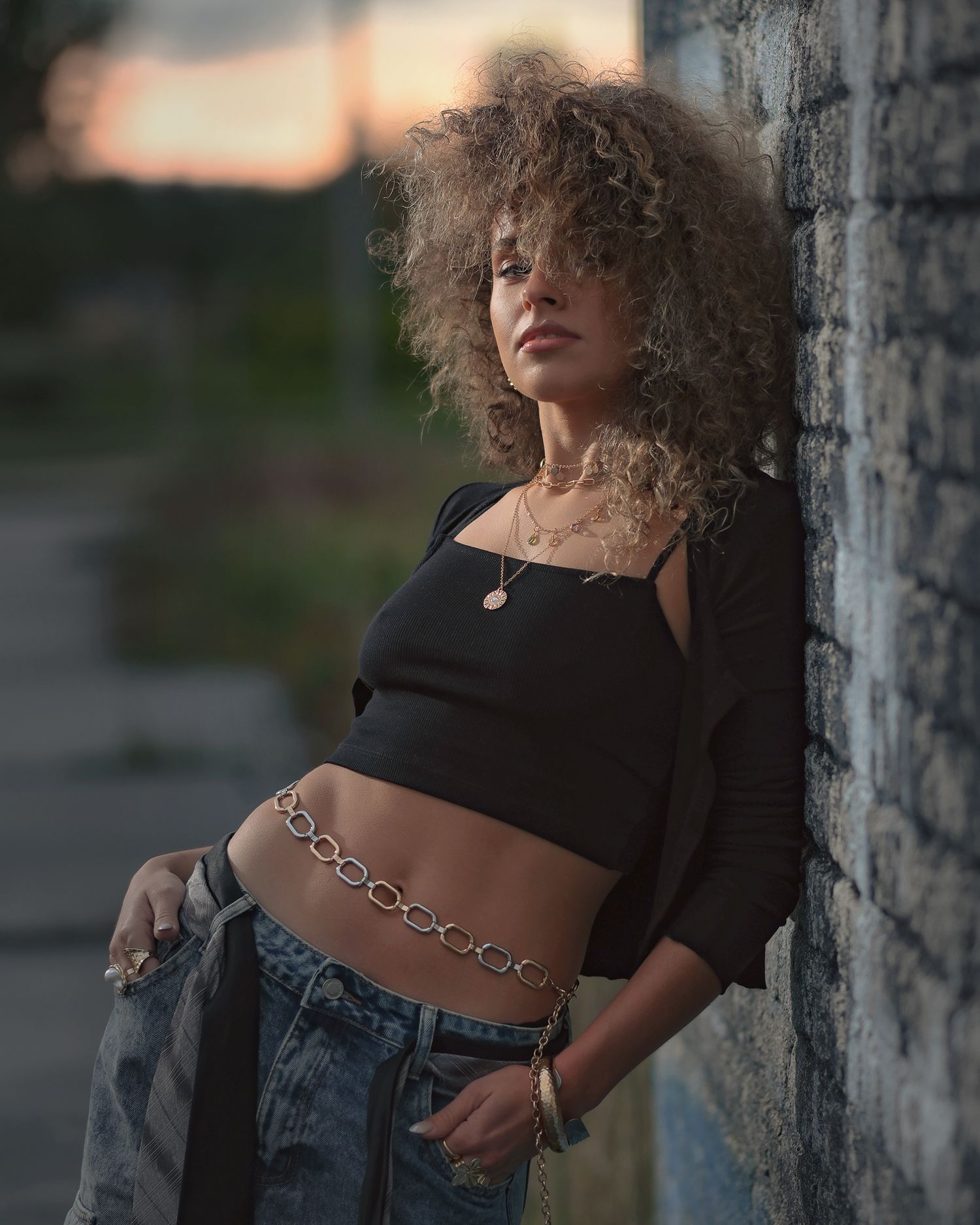 Global fashion photography: three-quarter portrait with moody lighting, model wearing layered gold necklaces and a chain belly belt.