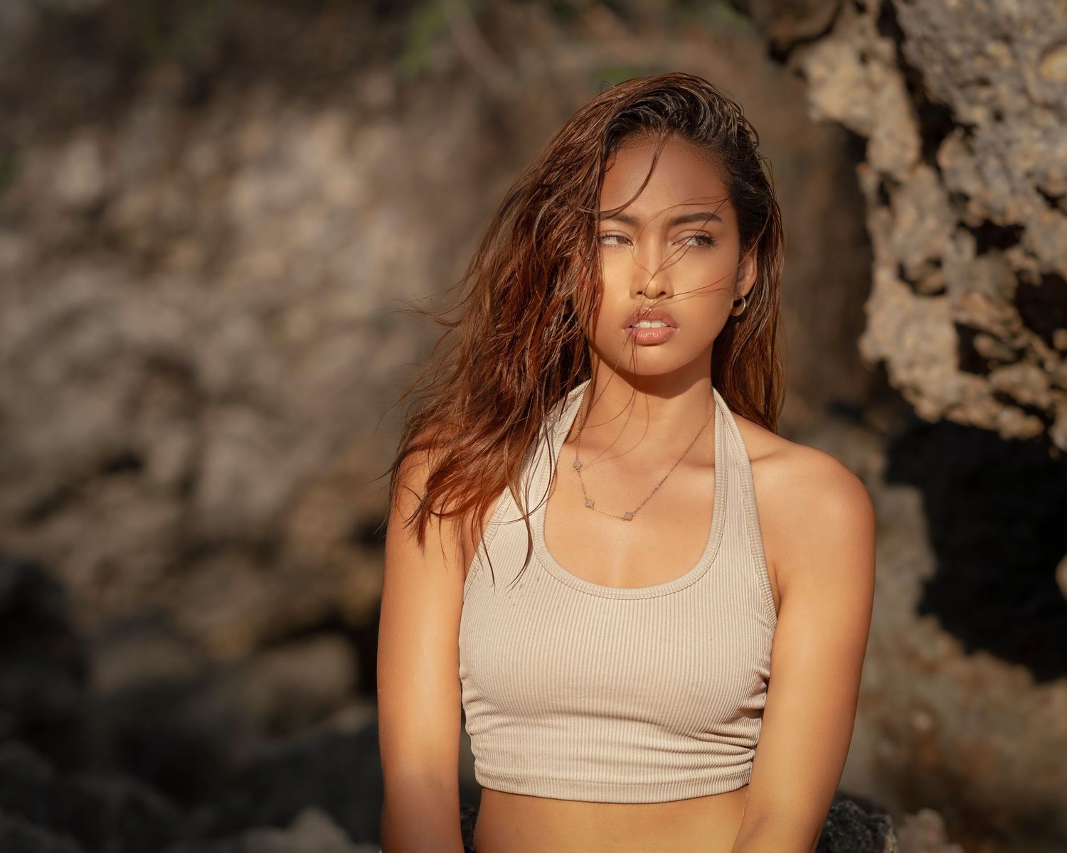Lifestyle portrait: model in ribbed crop top with sun-drenched skin, posing in a tropical rocky alcove, global fashion portfolio.