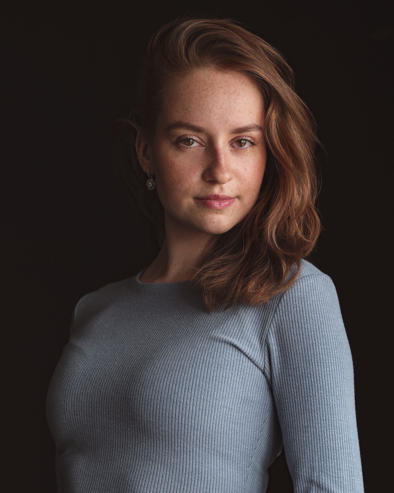 Natural light beauty portrait: close-up on freckled woman's face, warm lighting, blue ribbed top, global portfolio headshot.