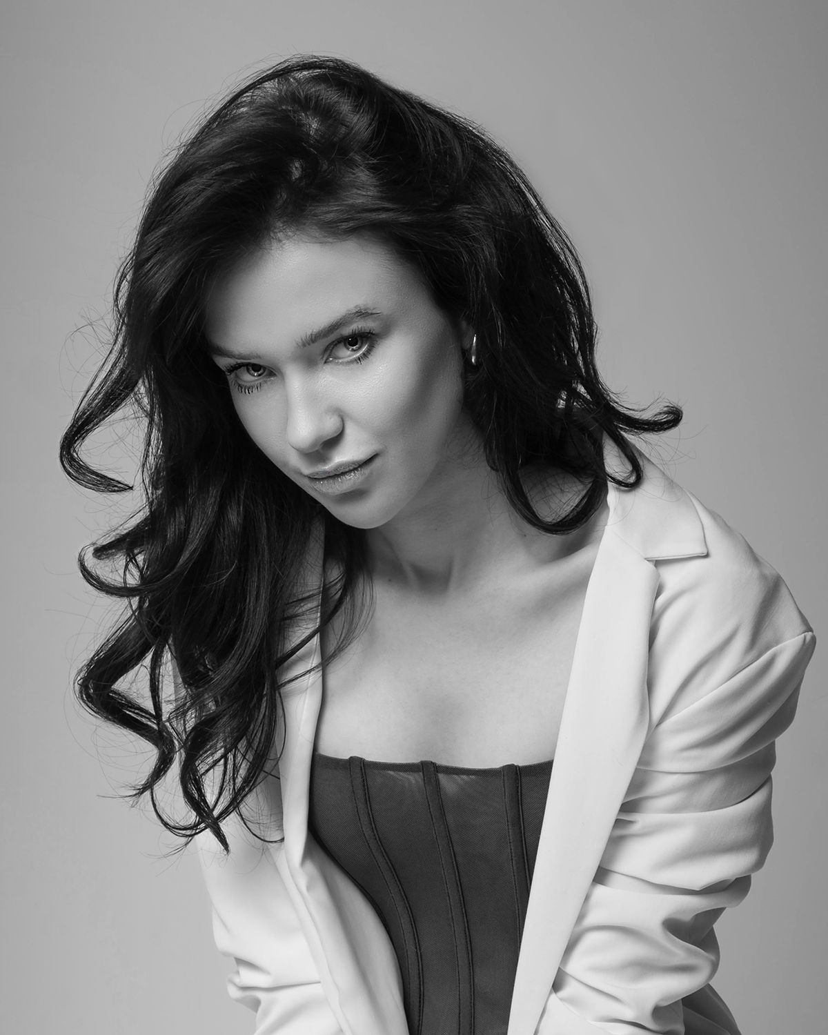 Editorial beauty portrait, monochrome: close-up on model with wavy hair, white jacket, intense gaze, global portfolio.
