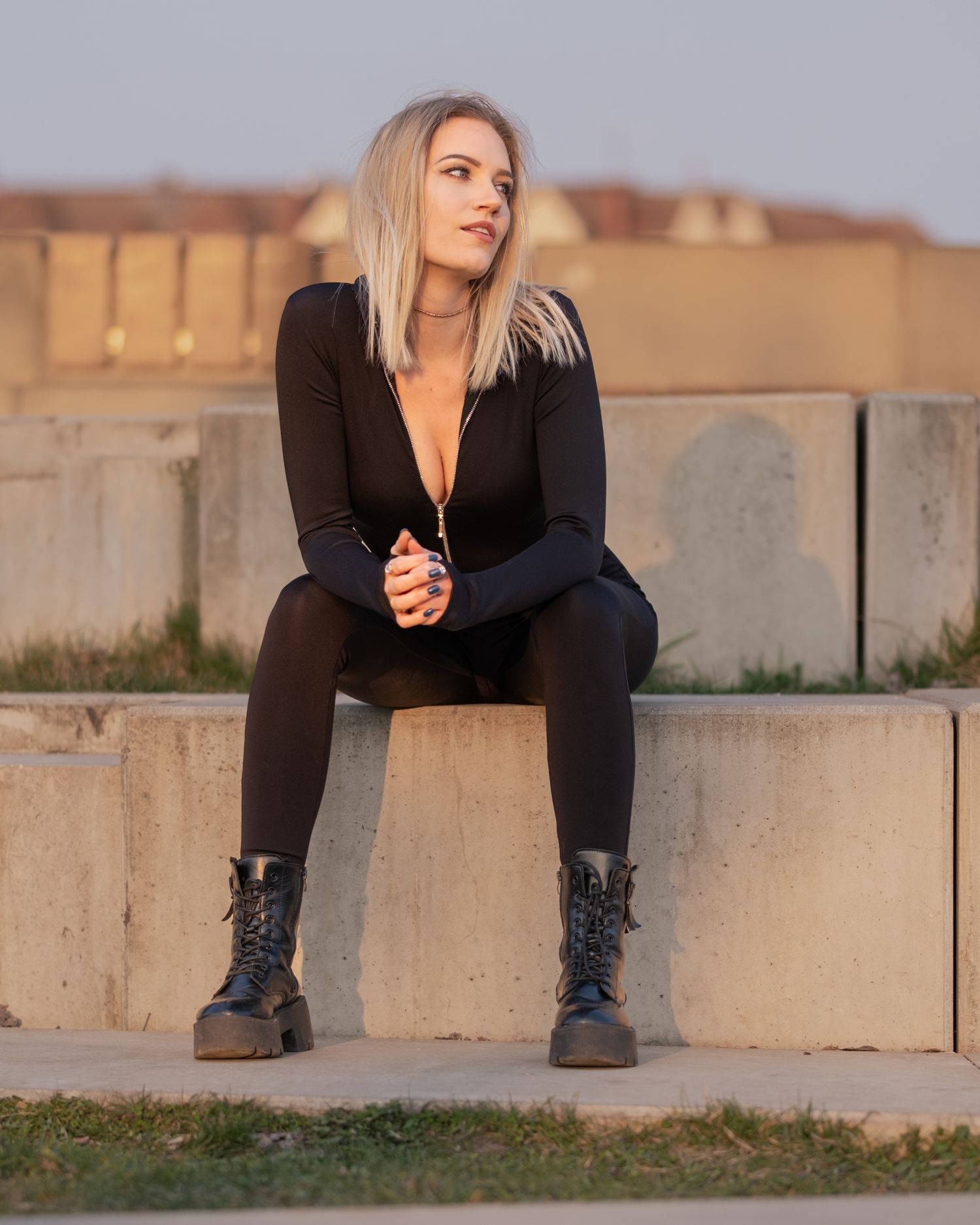 High-fashion contrast: model in black bodysuit and boots sits on a concrete step, urban aesthetic, cinematic light, global portfolio.